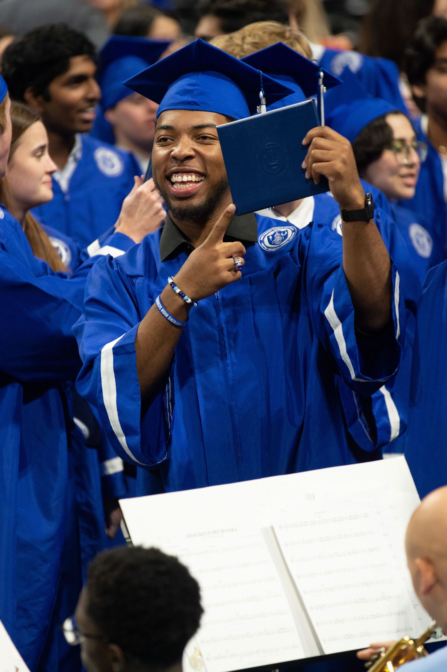 Graduate celebrates with diploma during commencement ceremony wearing blue regalia.