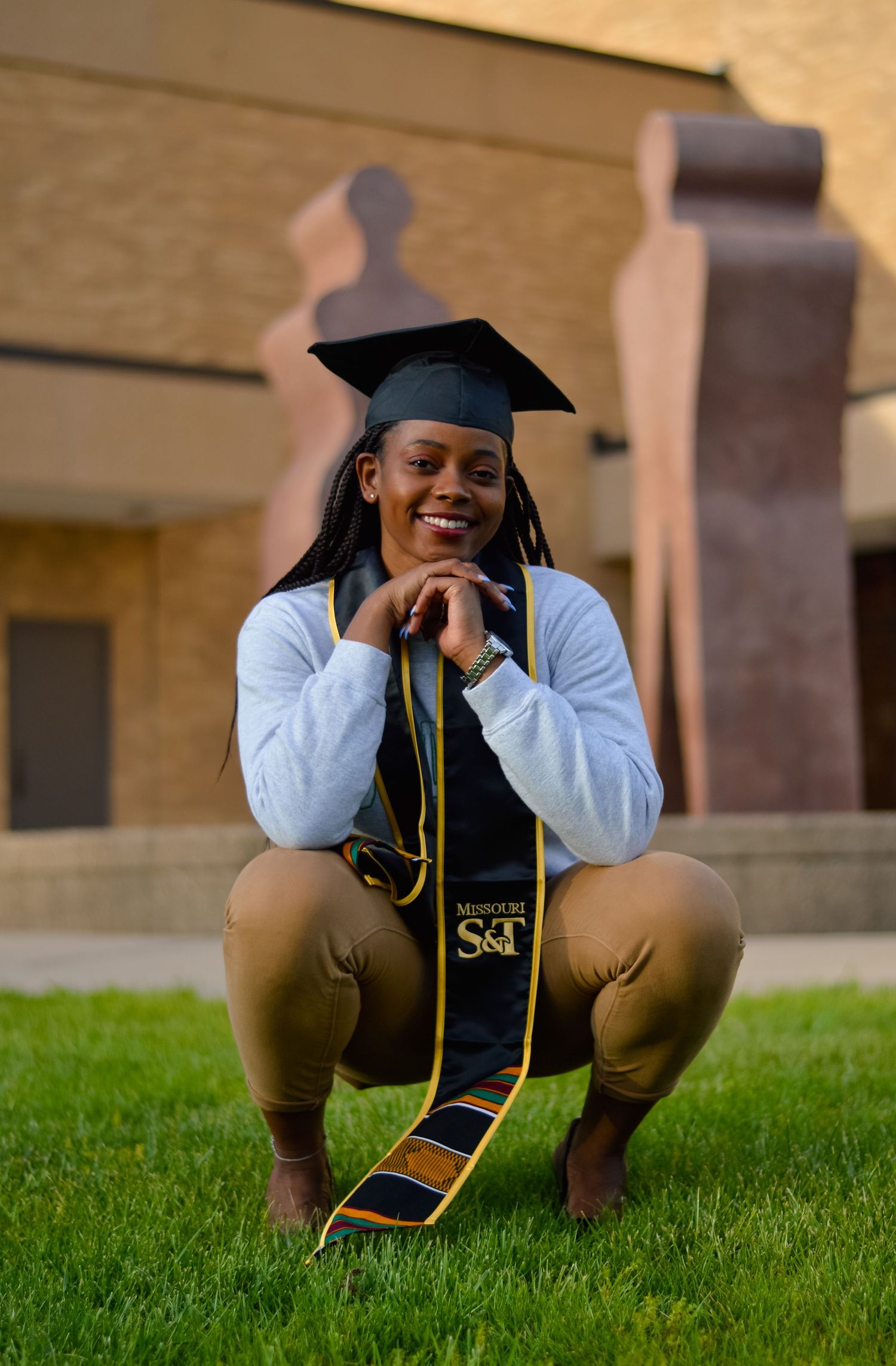 Graduate in academic regalia posing playfully on grass during photo session.