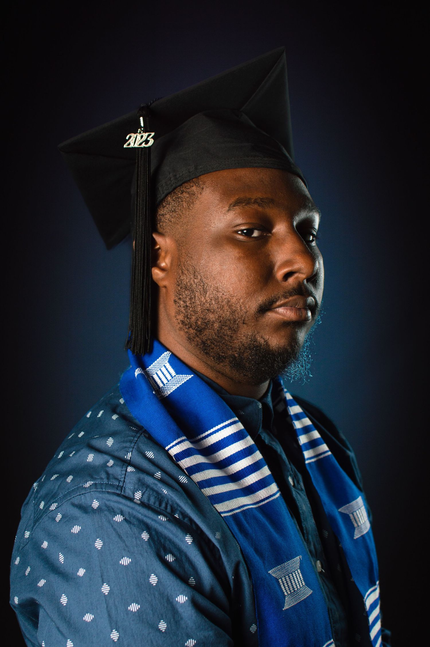 Graduate portrait series showing person in graduation cap and blue striped stole against dark backdrop.