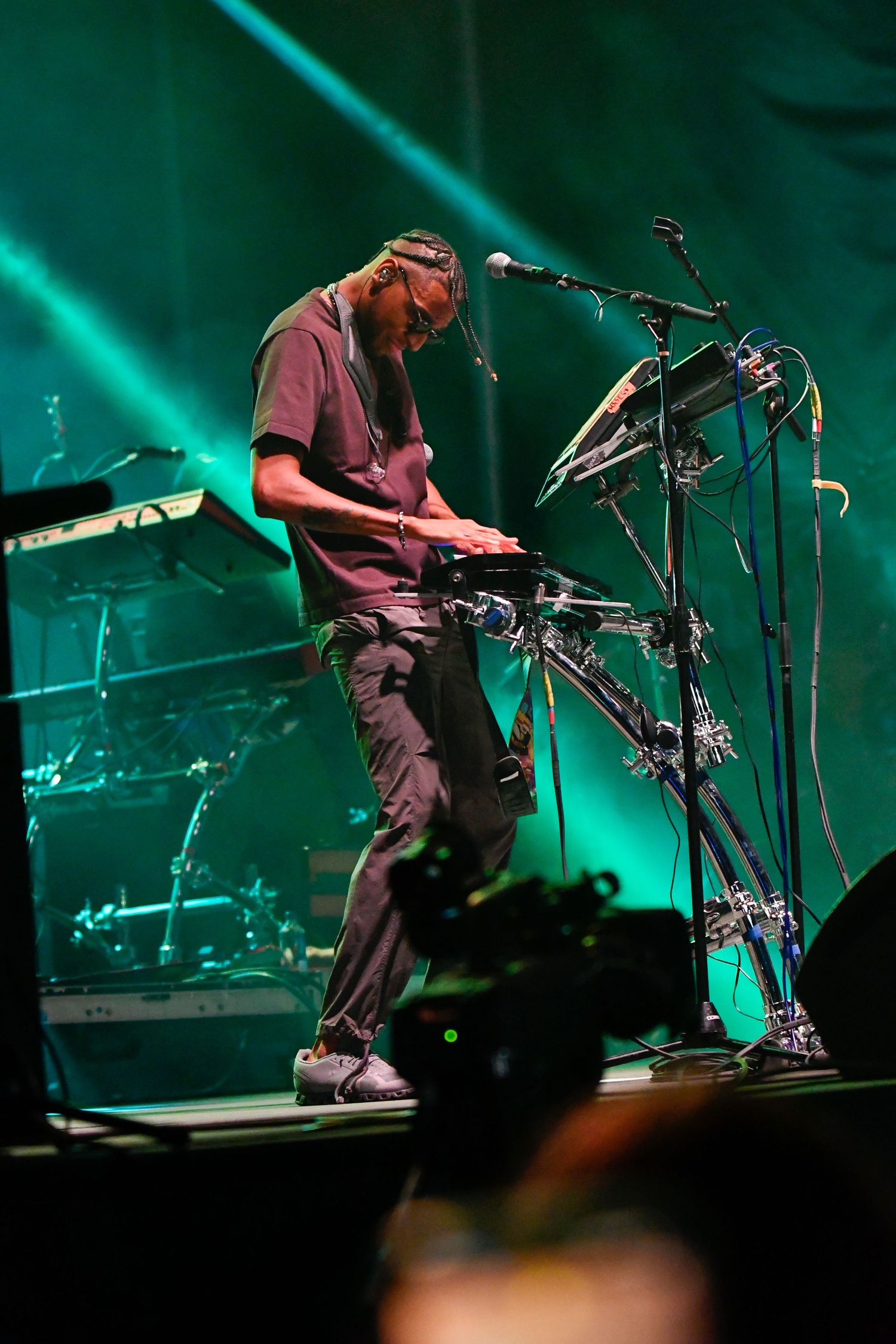 Musician performs on stage with electronic drum setup under dramatic teal lighting during live concert performance.