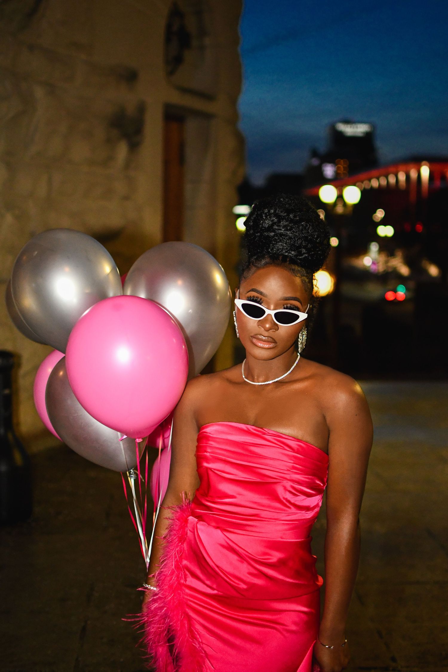 Evening photoshoot featuring bright pink dress and silver balloons against urban backdrop.