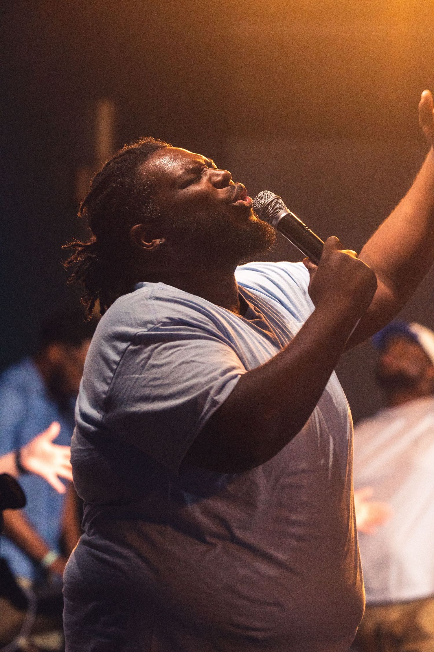 A gospel singer performs passionately on stage in a blue shirt against warm lighting during a worship service.