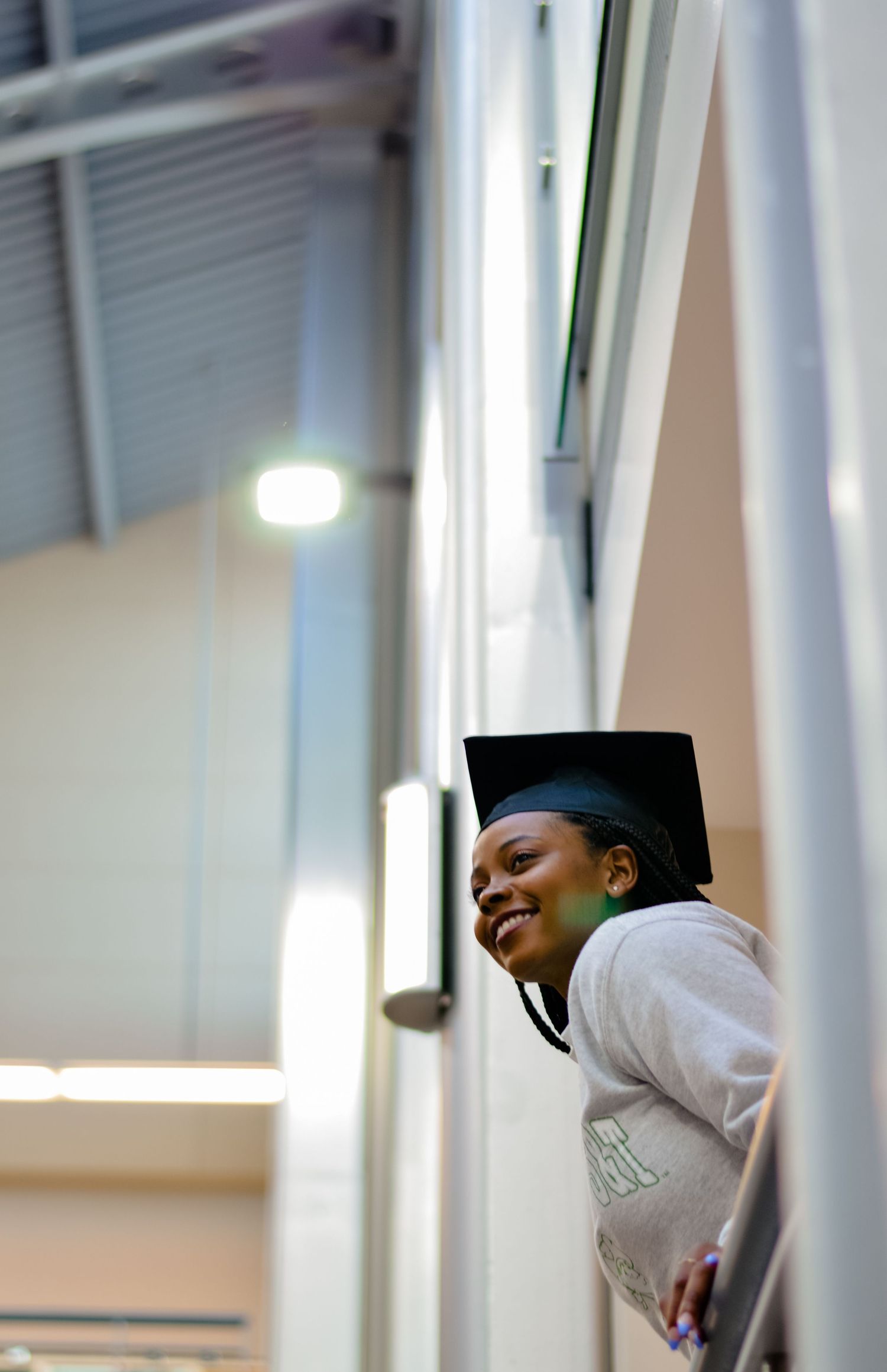 Graduate in cap and gown smiling through window reflection.