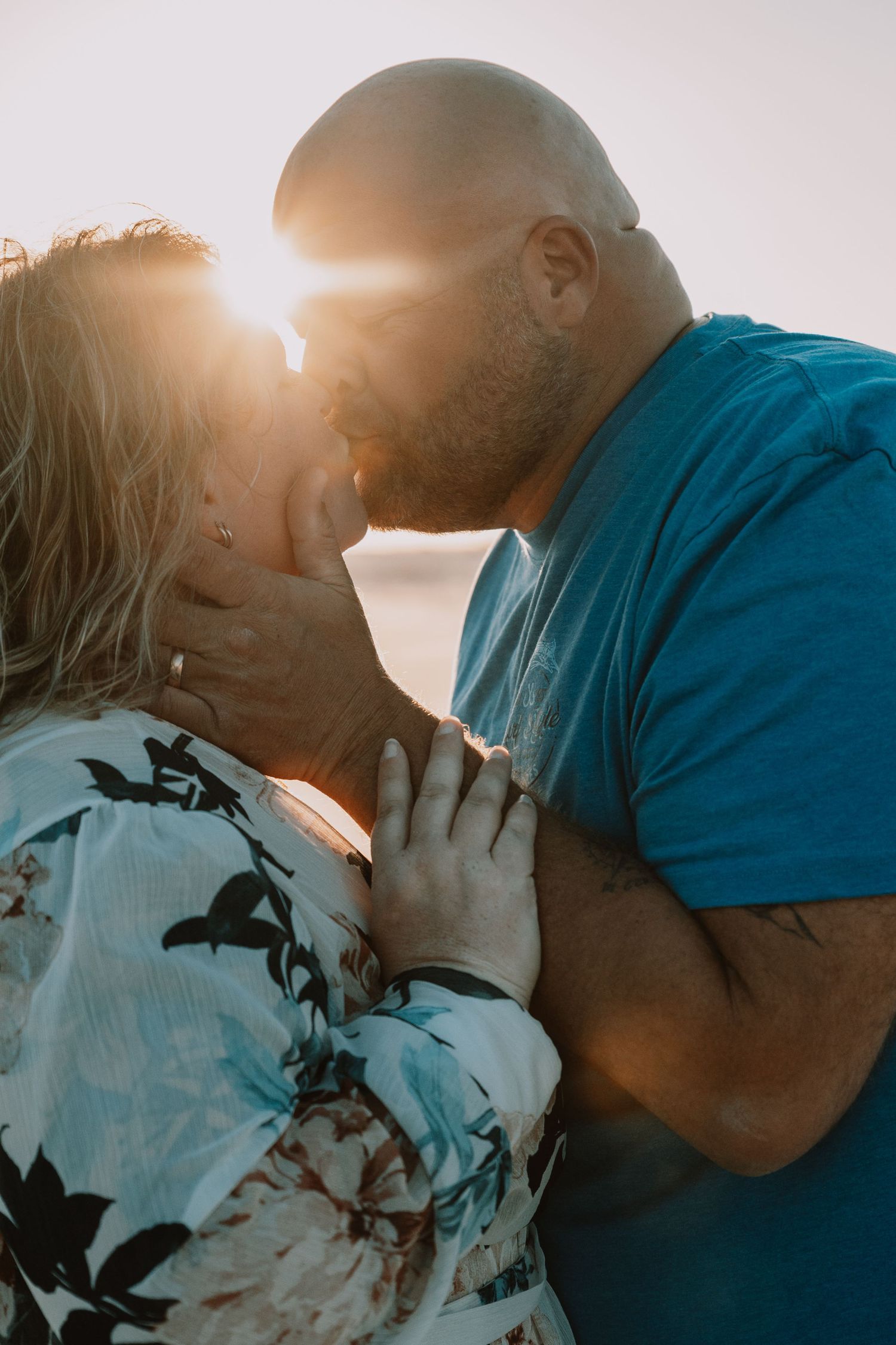 Couple shares a passionate kiss backlit by a stunning golden sunset at the beach.
