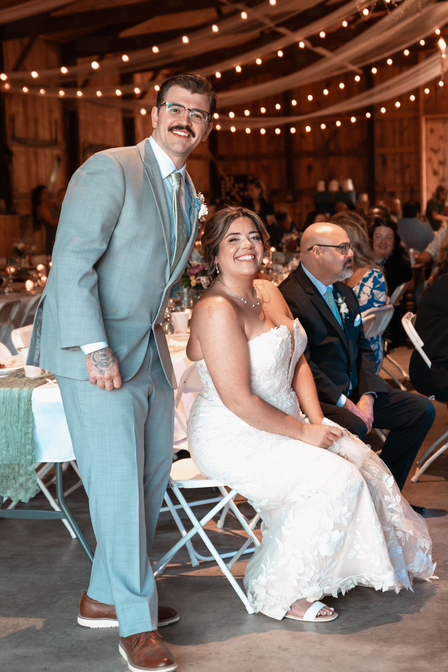 Smiling bride and groom posing at reception in warmly lit barn venue.