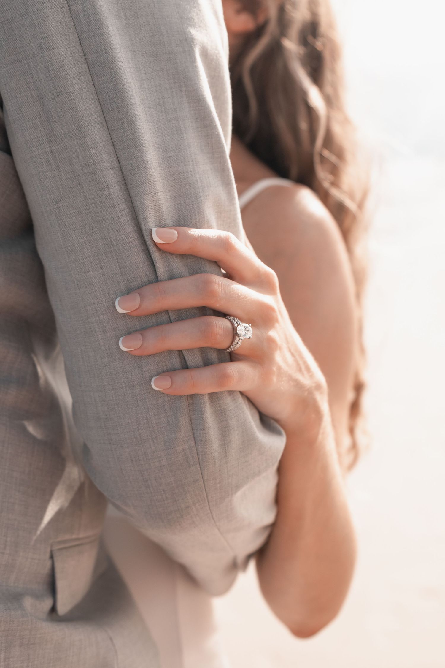 Close-up of bride's hand with diamond engagement ring holding groom's gray suit jacket.