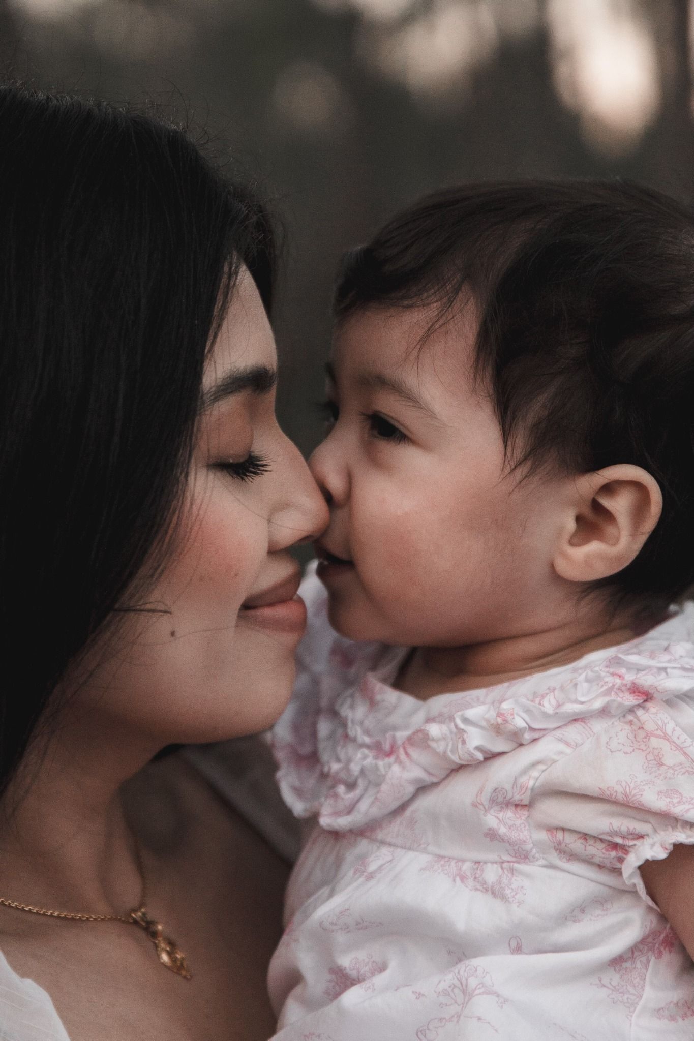 Asian mother and toddler girl share a sweet nose-to-nose moment in close-up portrait.