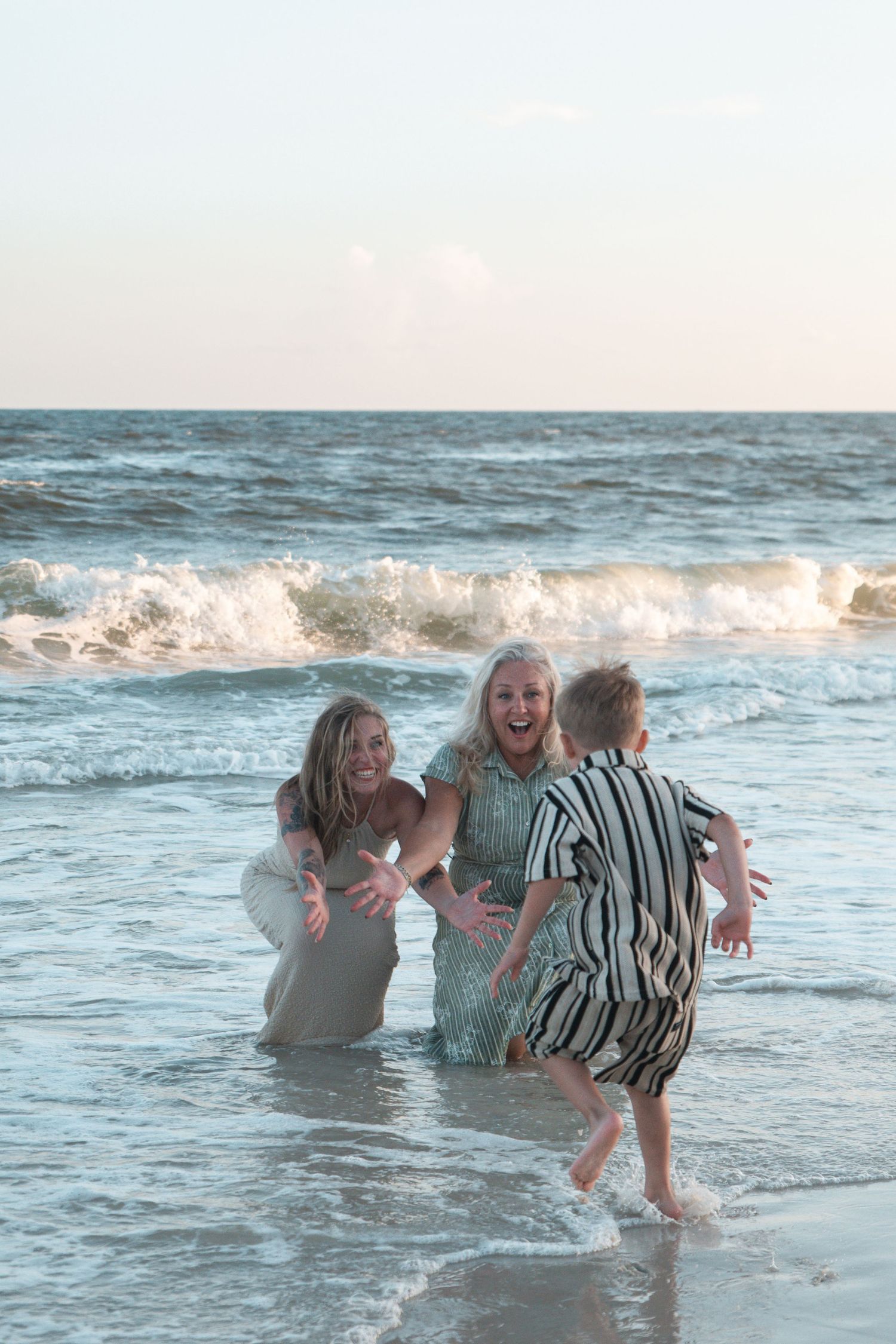 Two women and a child playing joyfully in ocean waves at the beach during golden hour.