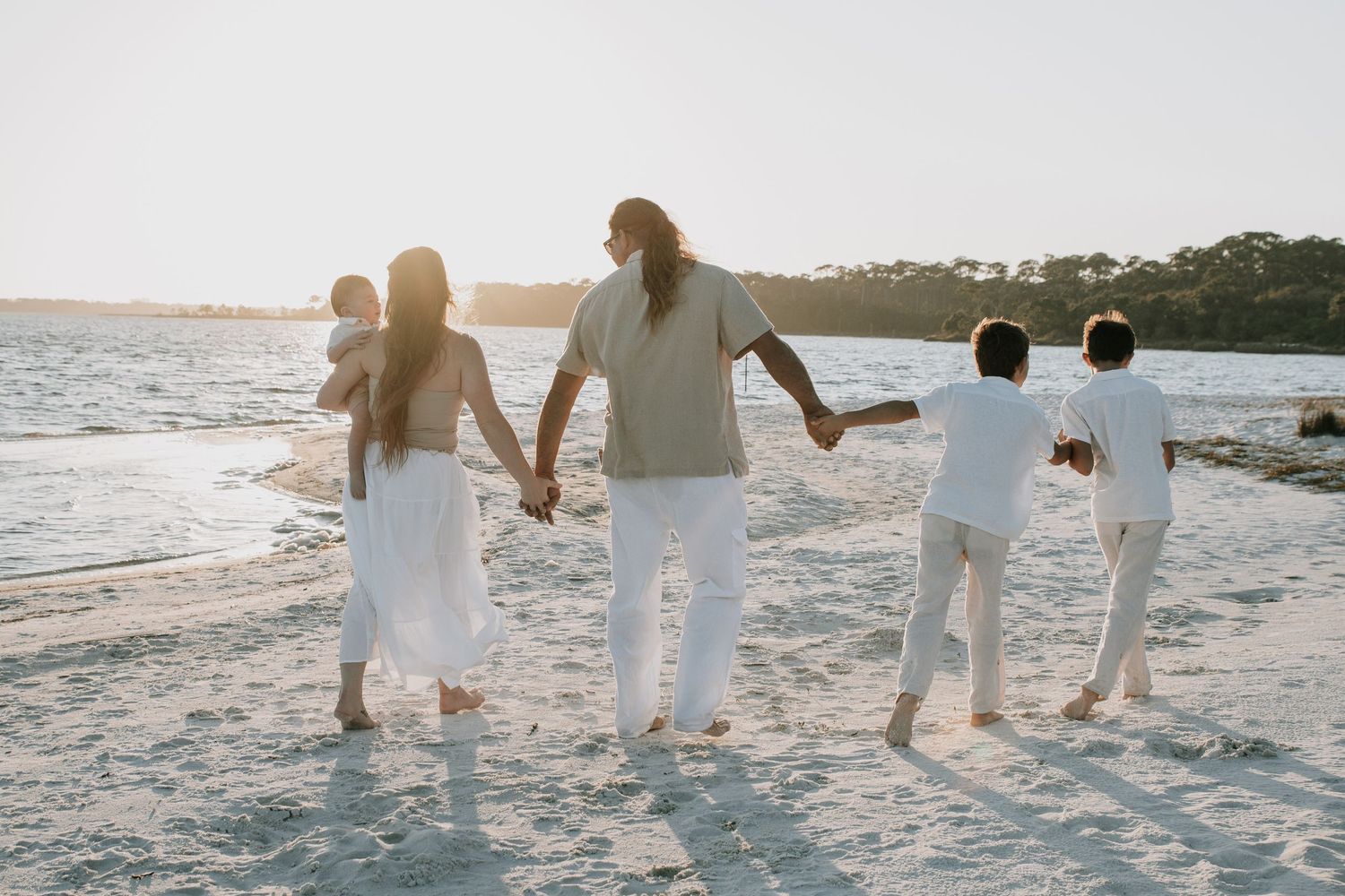 Family running together through the sand on the beach at sunset with joyful energy