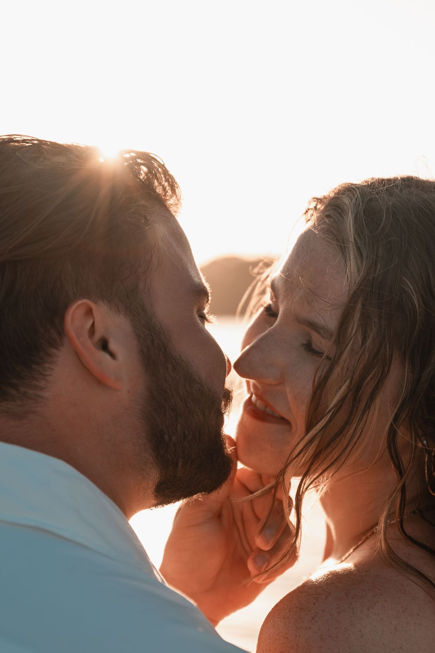 Close-up of couple about to kiss at sunset, man tenderly holding womans face in warm golden light.