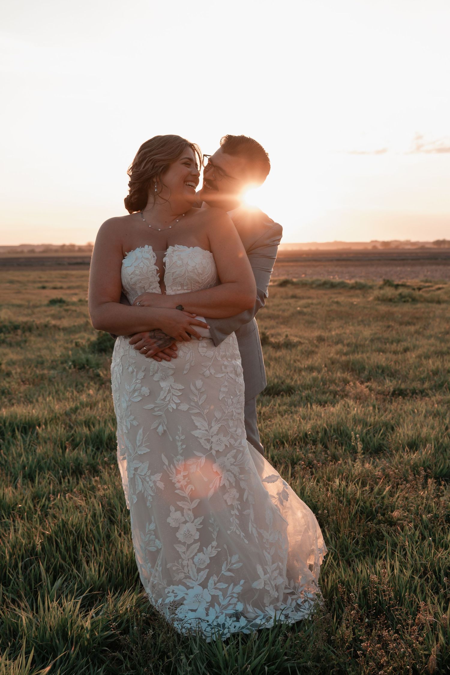 New wedding couple sharing a romantic embrace in an open Midwest field at golden hour