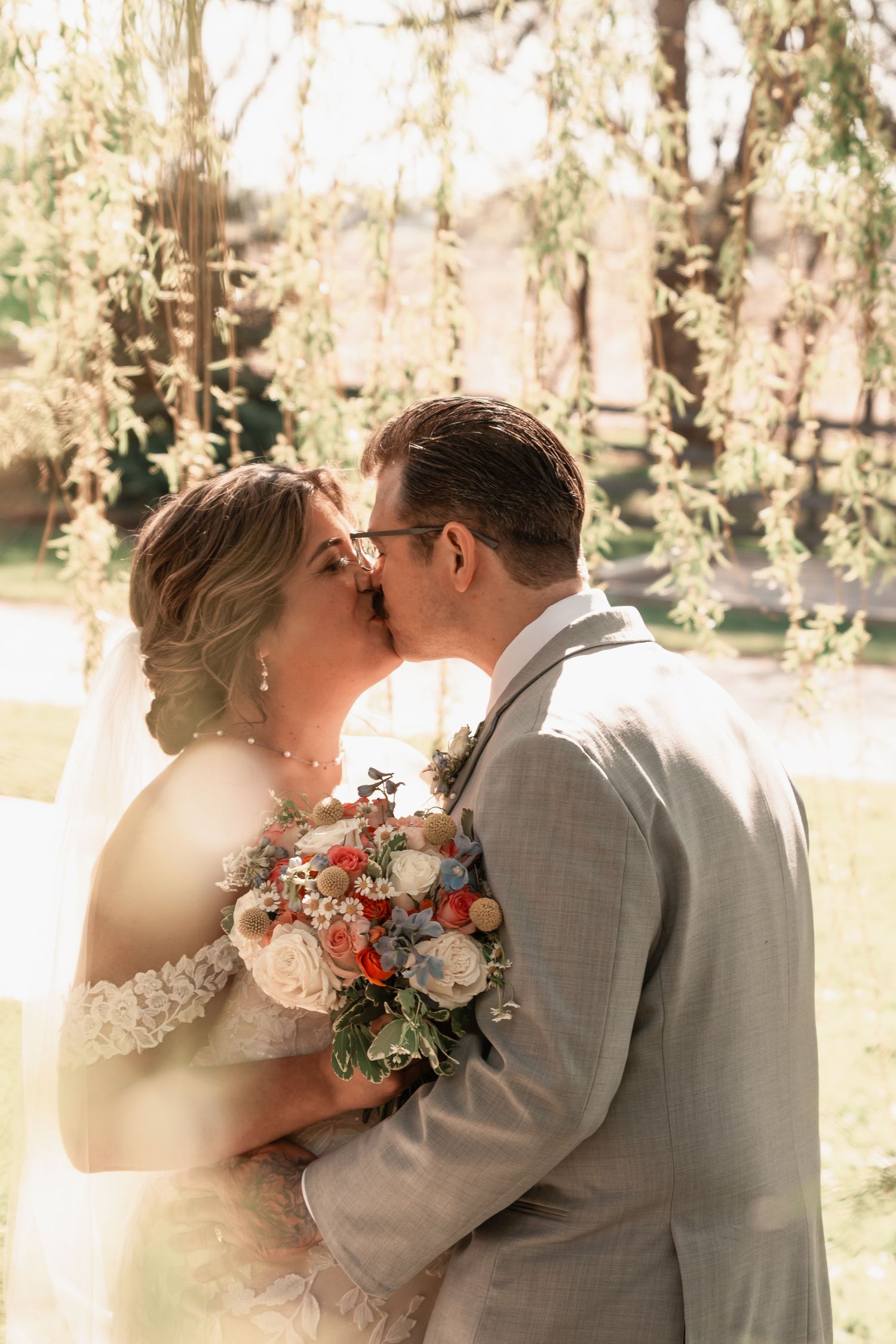 Dreamy bride and groom sharing a romantic moment beneath a willow tree at golden hour