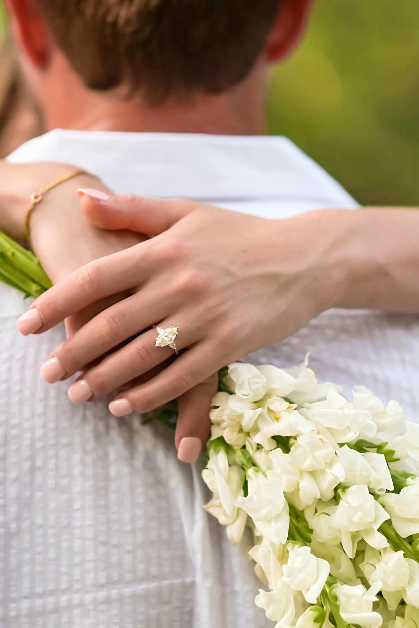 A bride displays her diamond engagement ring while holding a white floral bouquet.