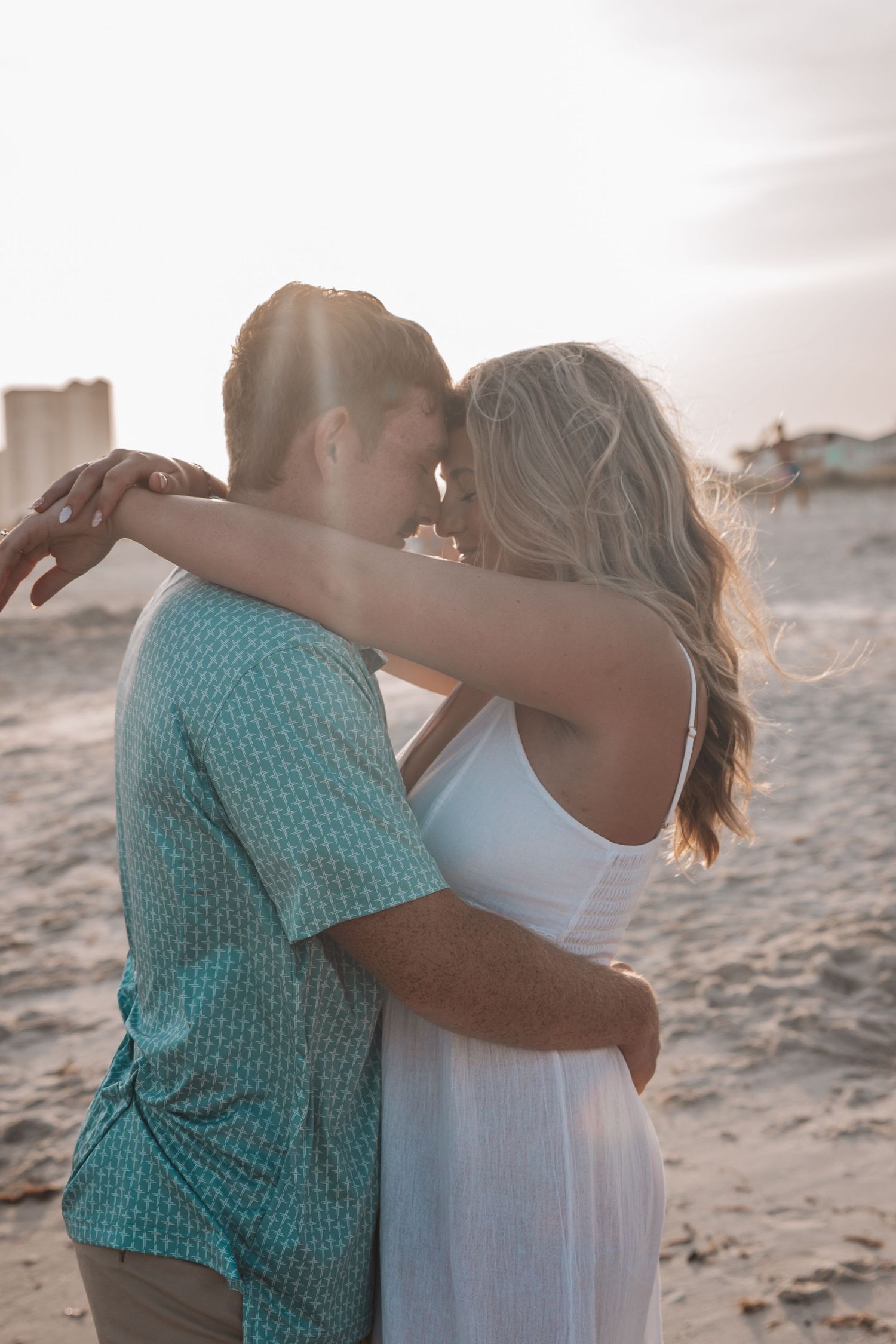 Couple embracing and sharing a romantic moment on a sandy beach at golden hour sunset.