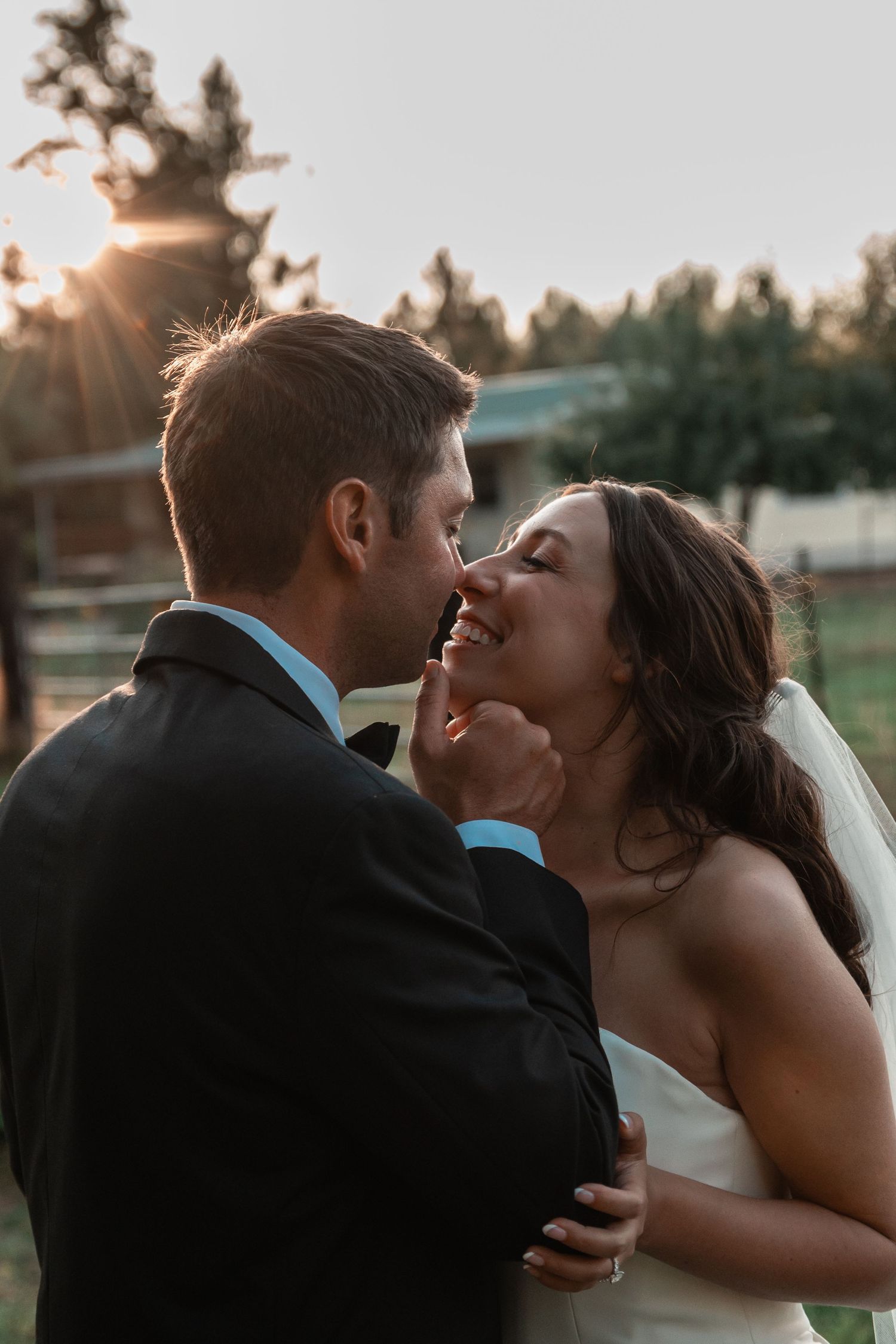 A bride and groom share a romantic moment at golden hour outdoors, with the smiling bride in a white gown and veil.