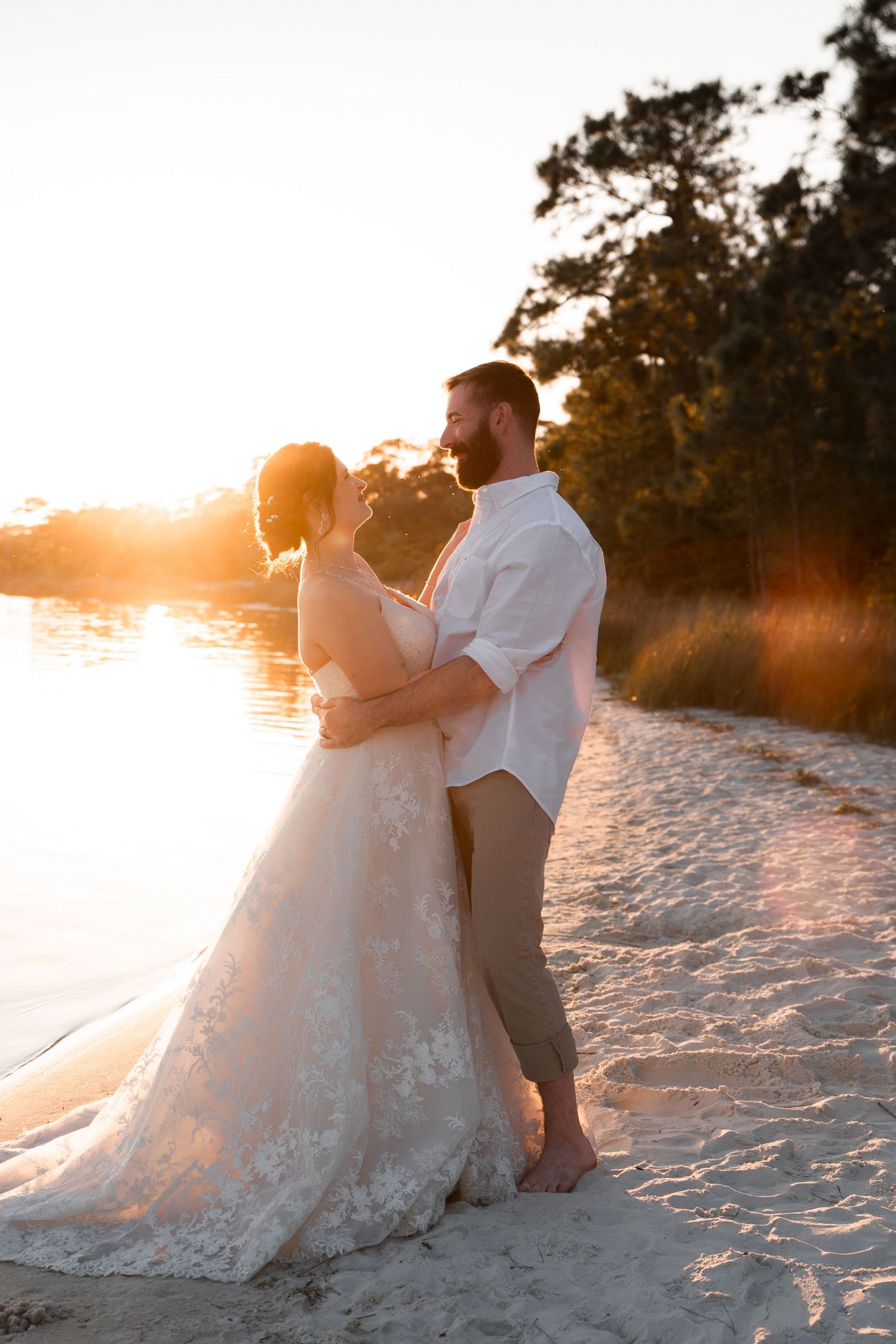 Romantic bride and groom holding each other on the beach during golden hour