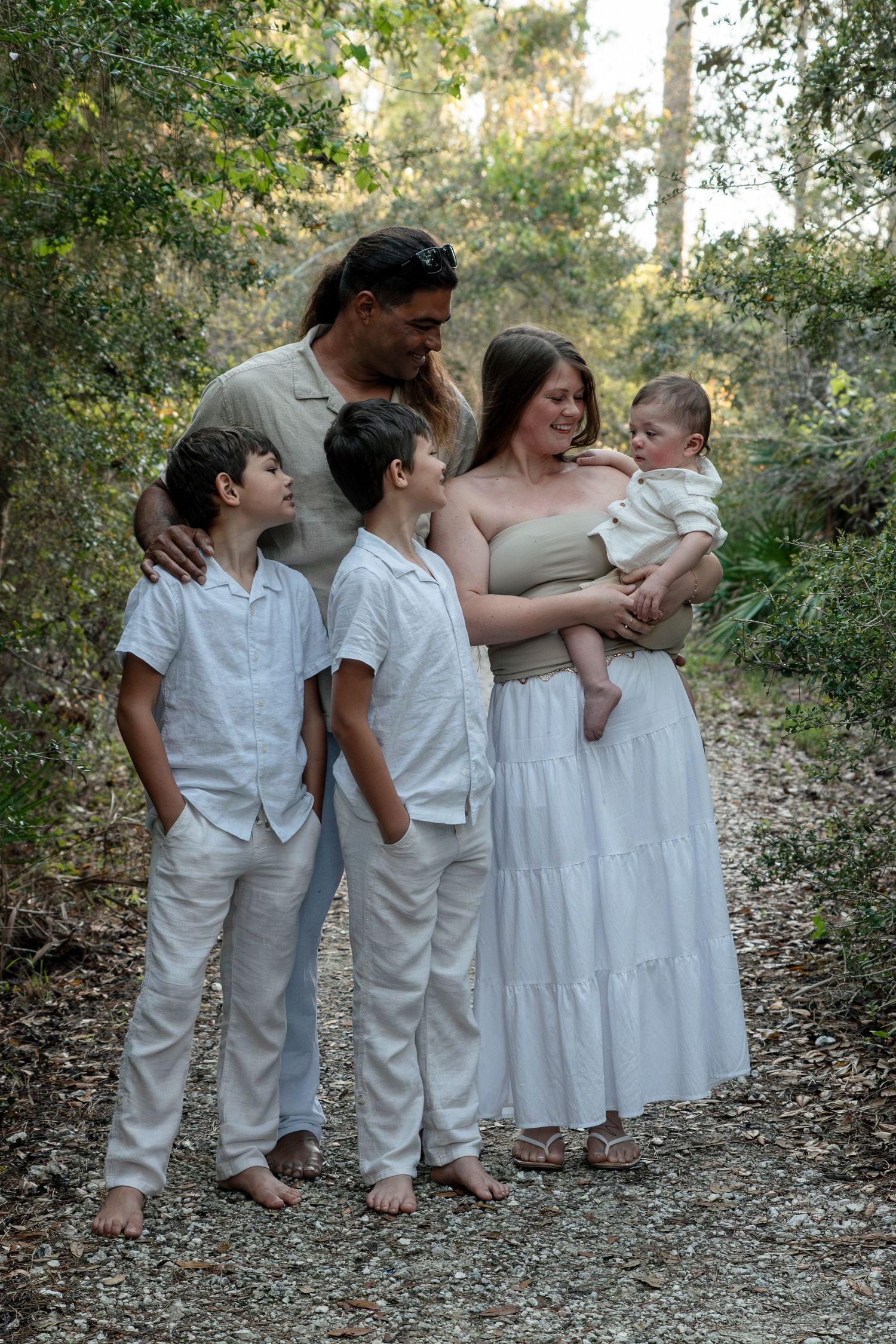 Happy family of five with father, mother, baby, and two boys posing on forest trail.