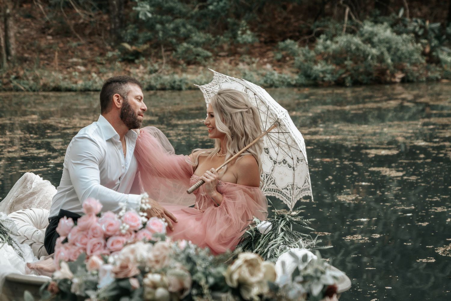 A couple shares a tender moment under a lace umbrella in a floral-decorated boat.