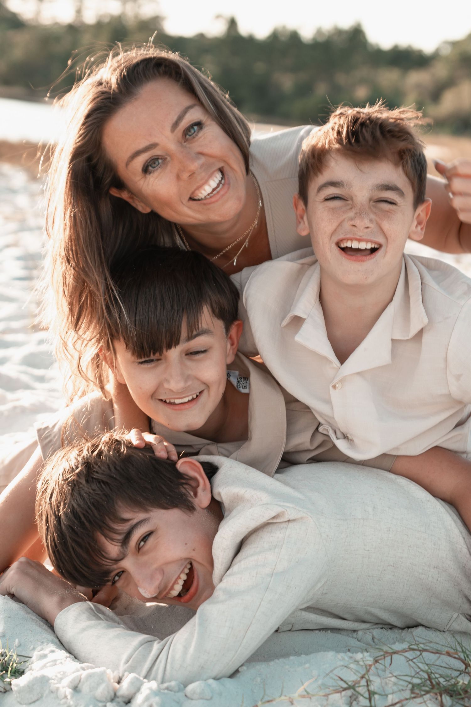 A joyful mother and three laughing boys cuddle together on a sunny beach blanket.