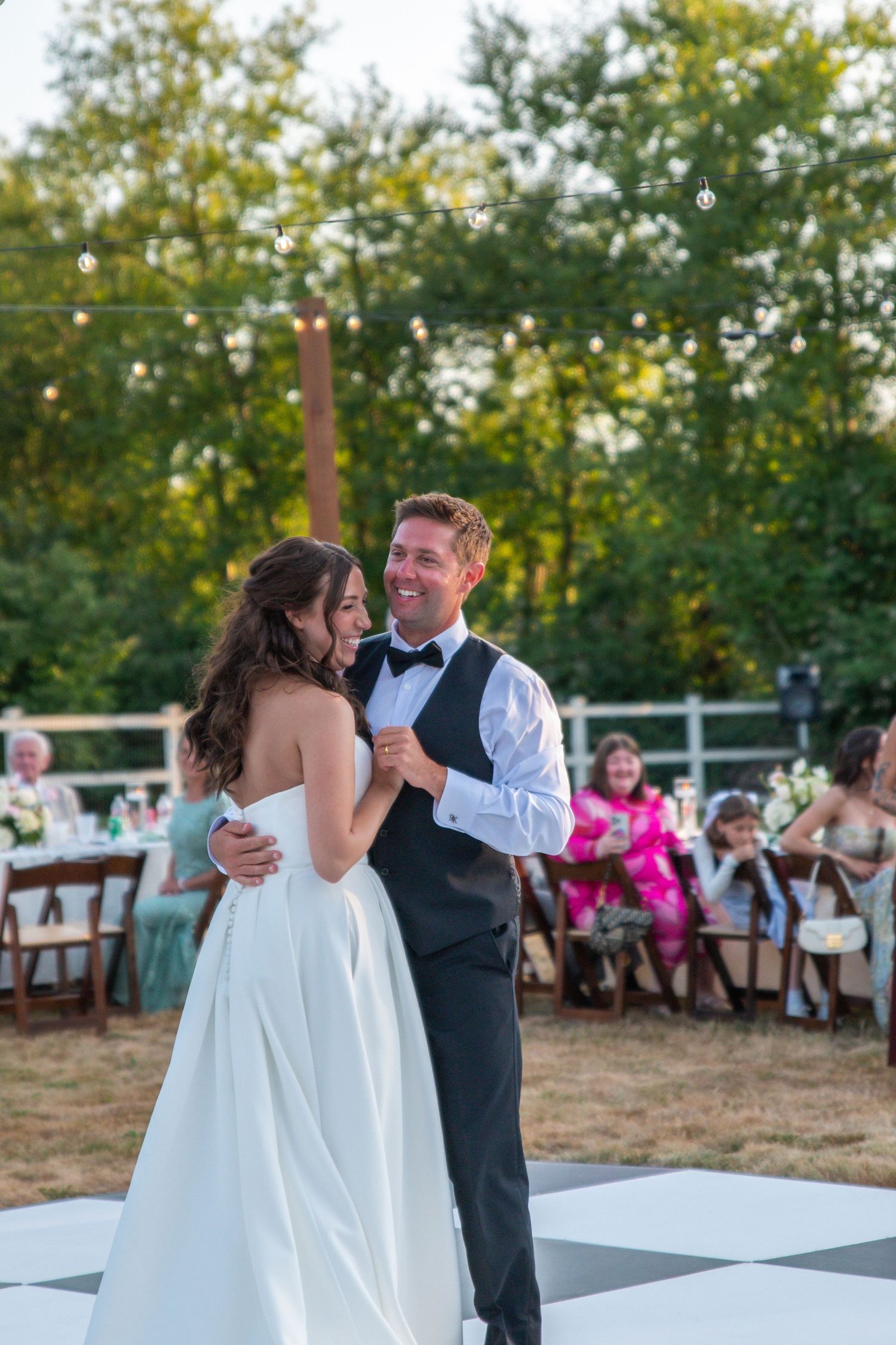 Bride and groom share their first dance on a checkered outdoor dance floor at a wedding reception.