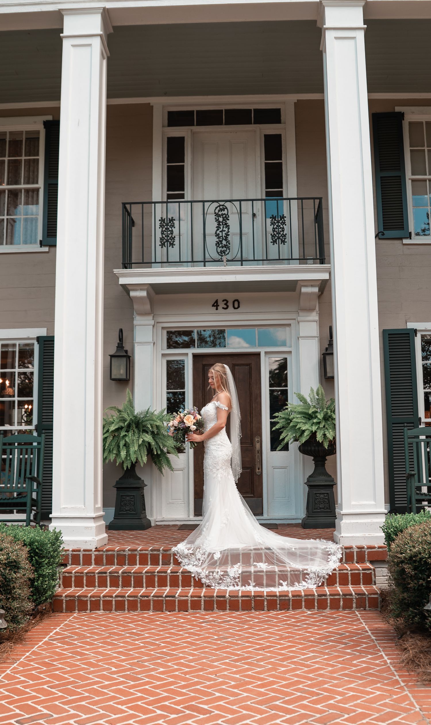 Bride in white mermaid gown with cathedral train poses on brick steps of elegant Southern colonial home numbered 430.