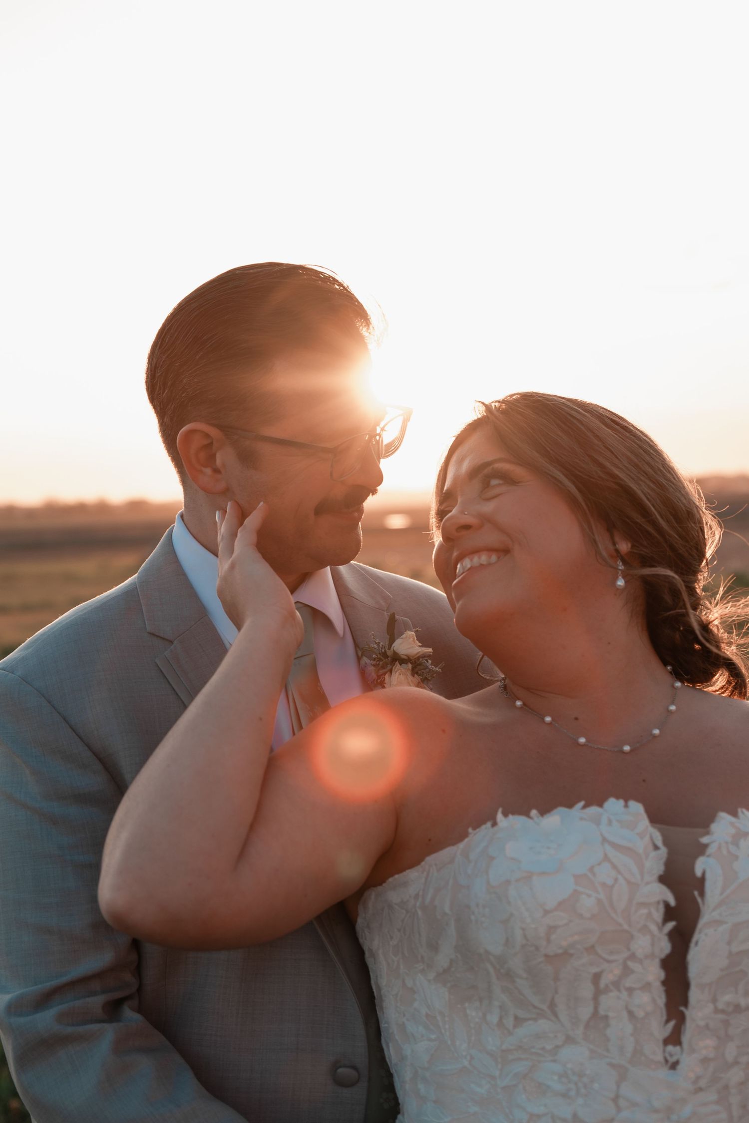 Romantic newlywed couple standing together in a wide open field with warm evening glow