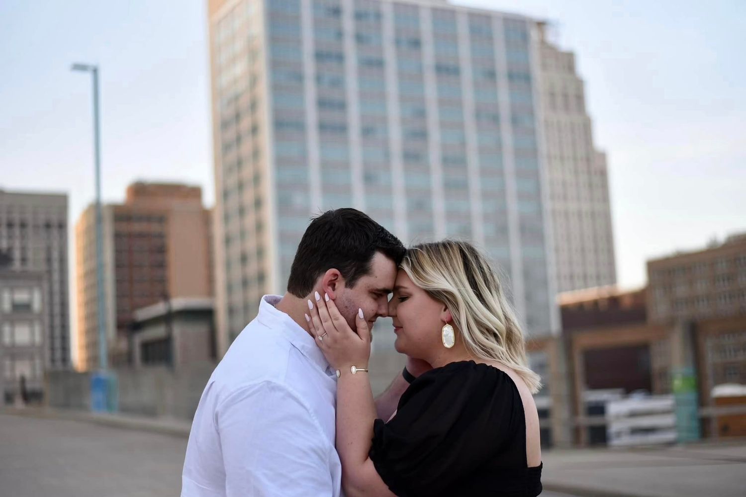 Couple tenderly touching foreheads in an intimate moment with a modern city skyline backdrop at sunset.