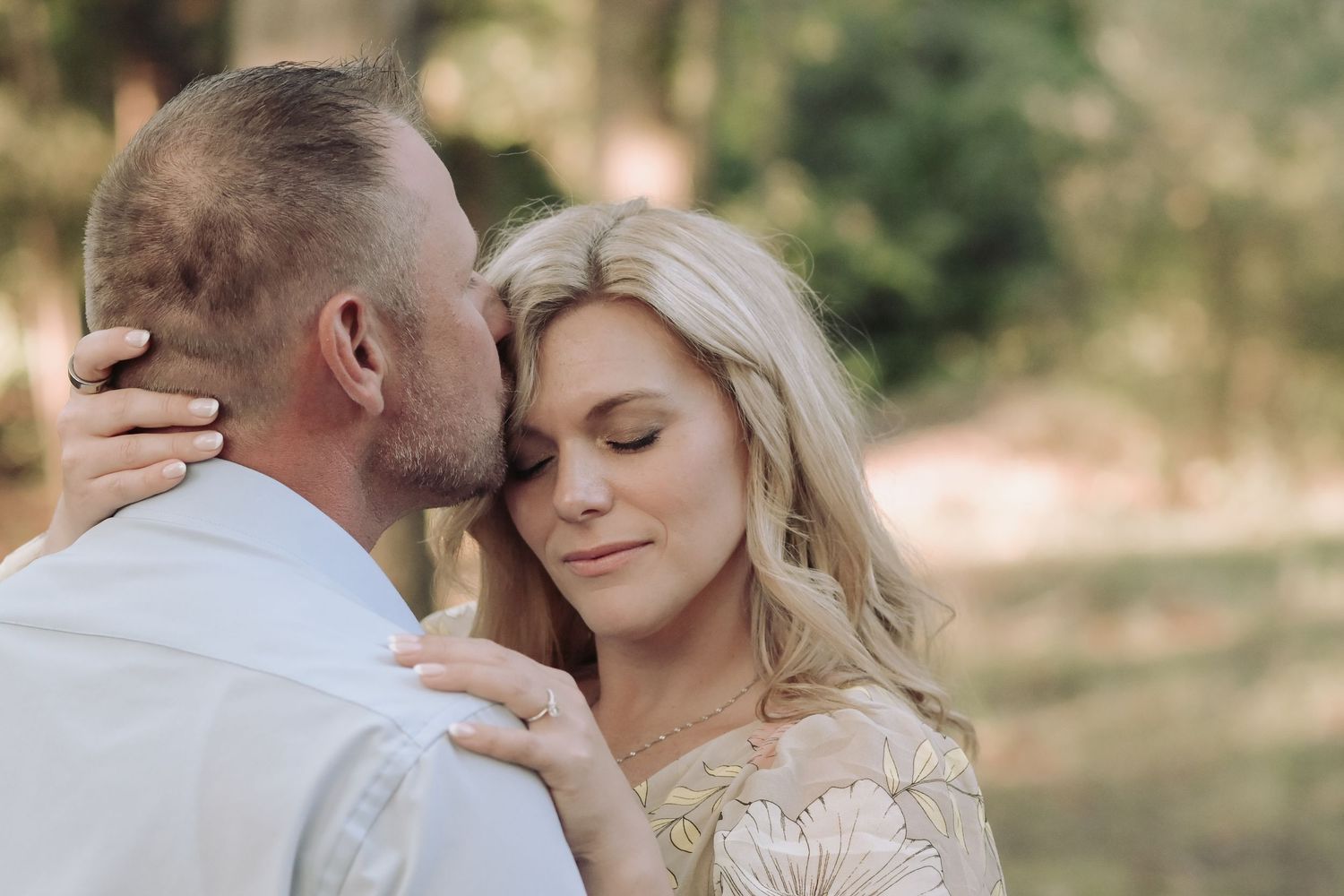 Close-up of couple sharing an intimate moment outdoors, woman smiling serenely as man kisses her cheek.