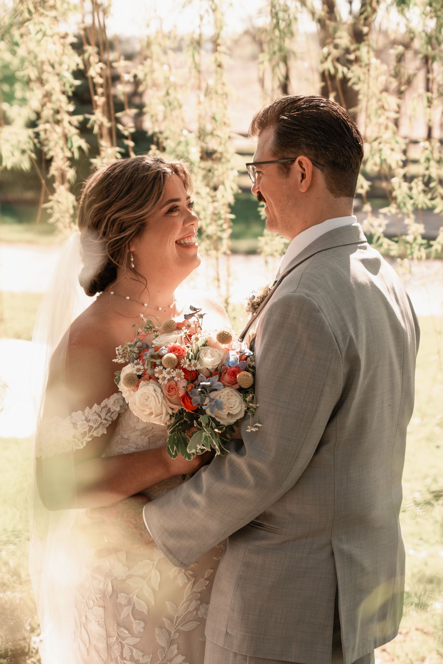 Intimate wedding couple embracing under a sweeping willow in a peaceful countryside setting