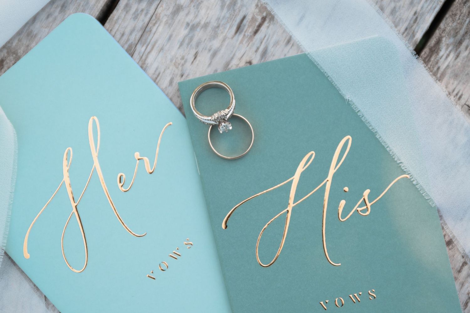 Gold foil his and her vow books in teal with diamond wedding rings on top.