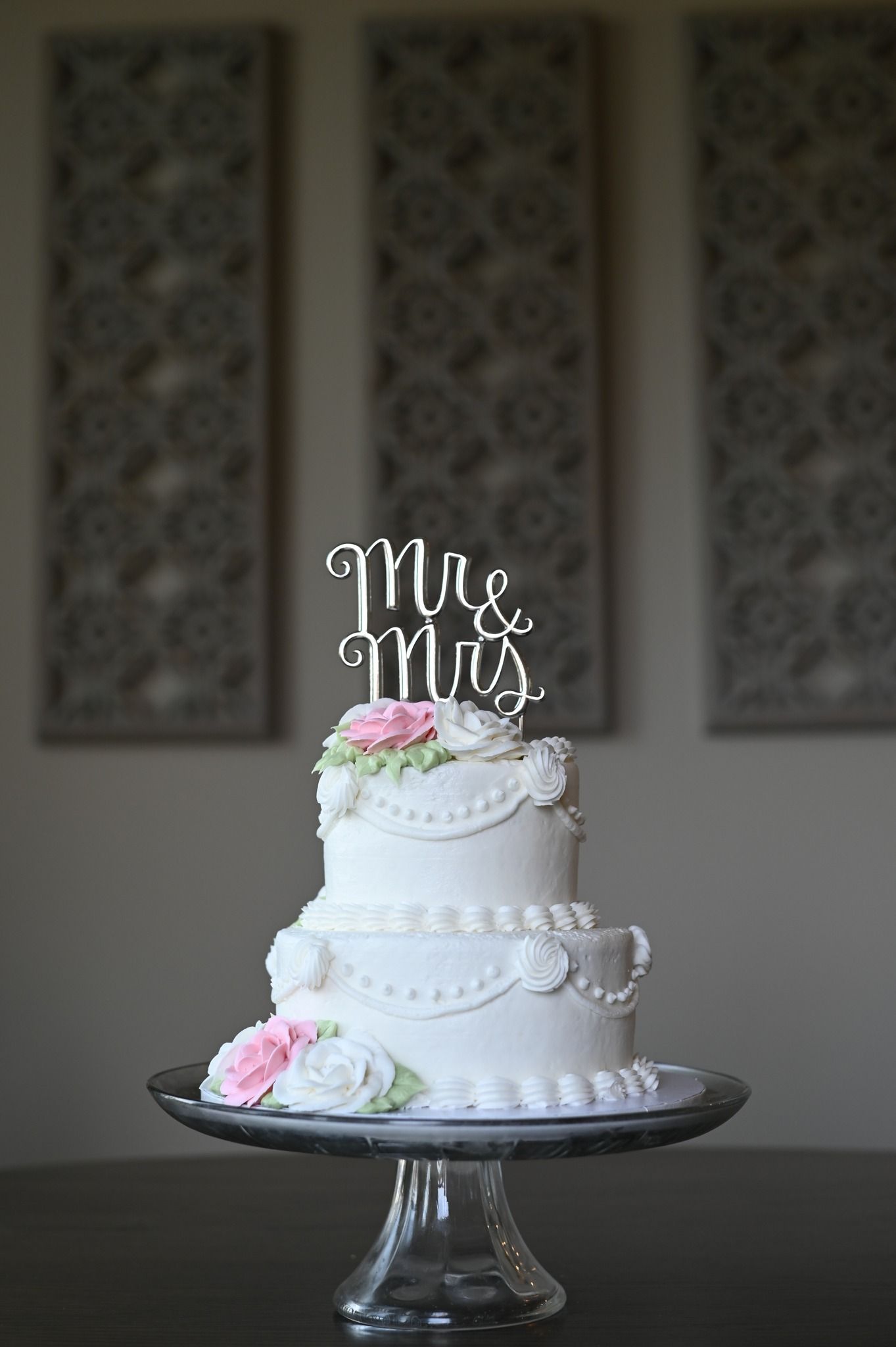 Elegant two-tier white wedding cake with Mr and Mrs topper adorned with pink and white sugar roses.