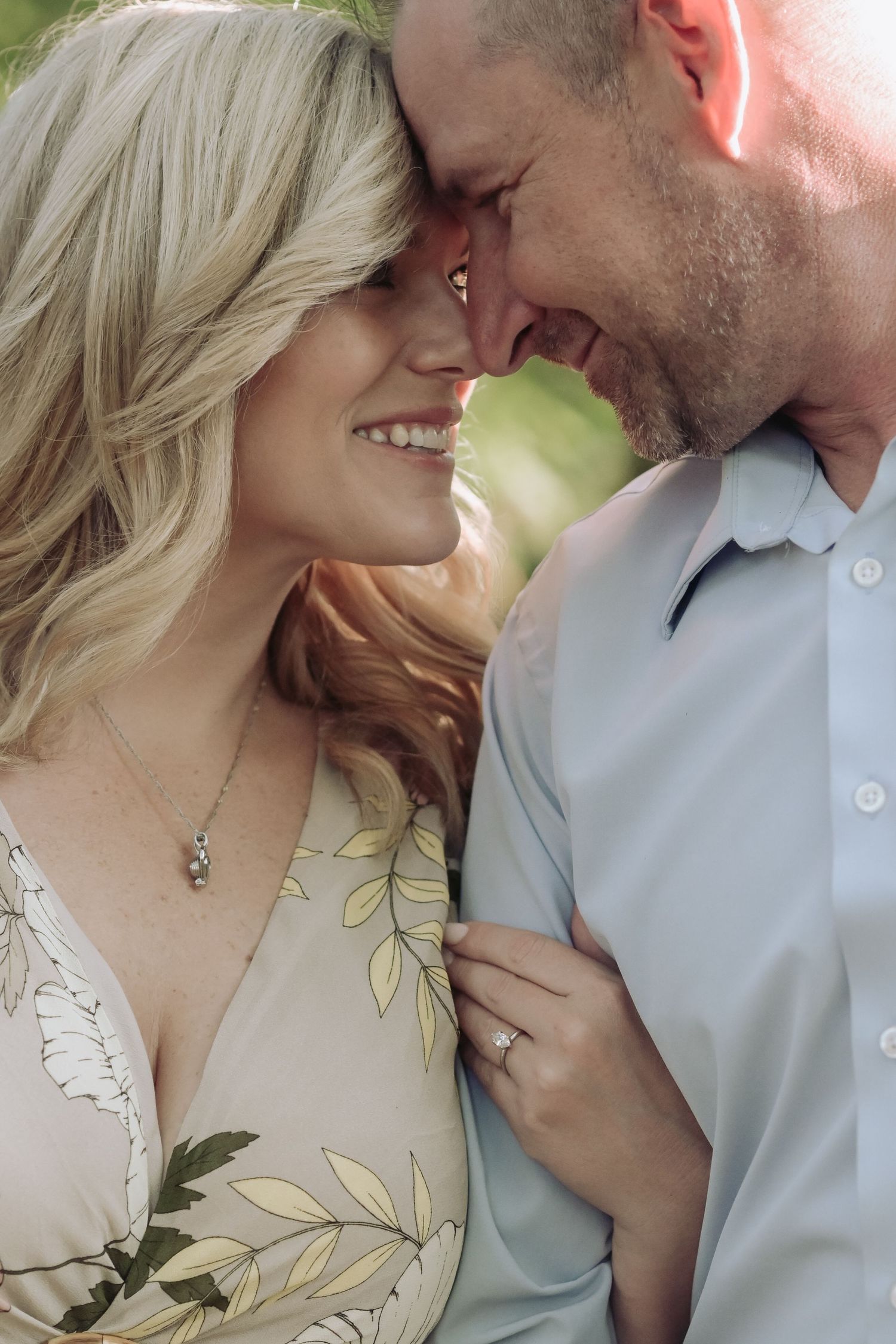 Happy engaged couple smiling and touching foreheads, woman displaying diamond ring while holding man's arm.