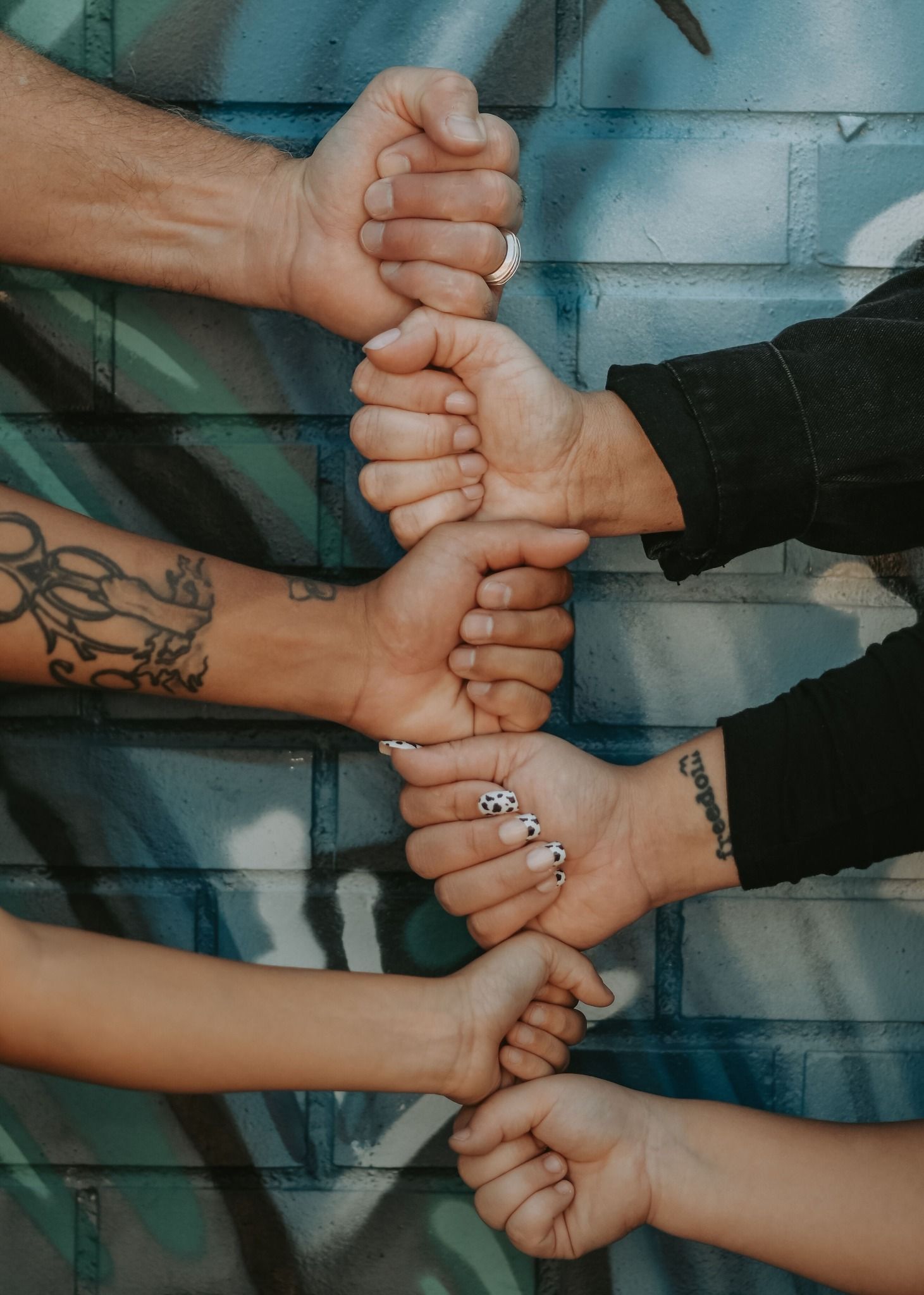 Four people form a chain of fist bumps against a colorful graffiti wall outdoors.