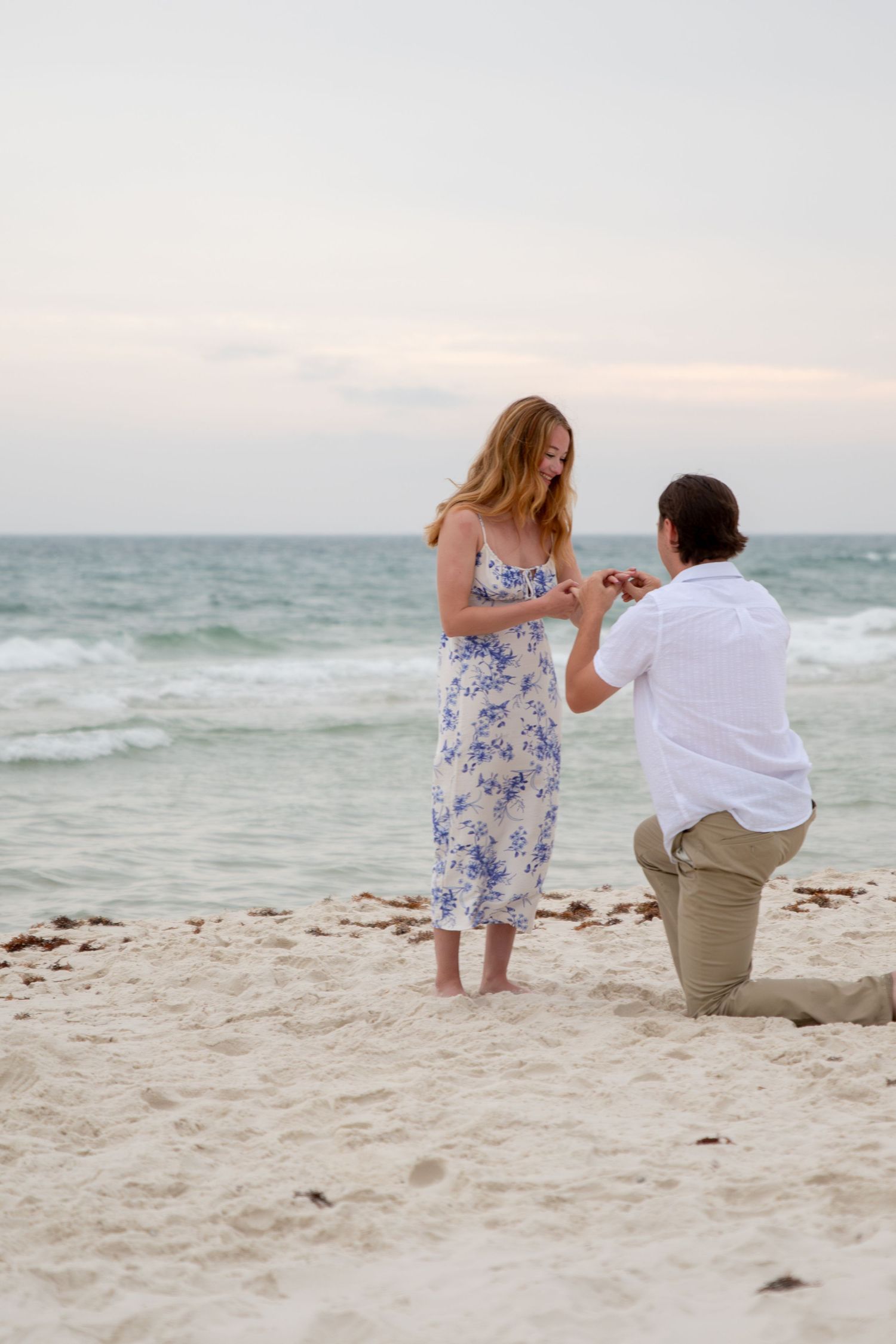Young couple during surprise beach proposal at golden hour on the shoreline