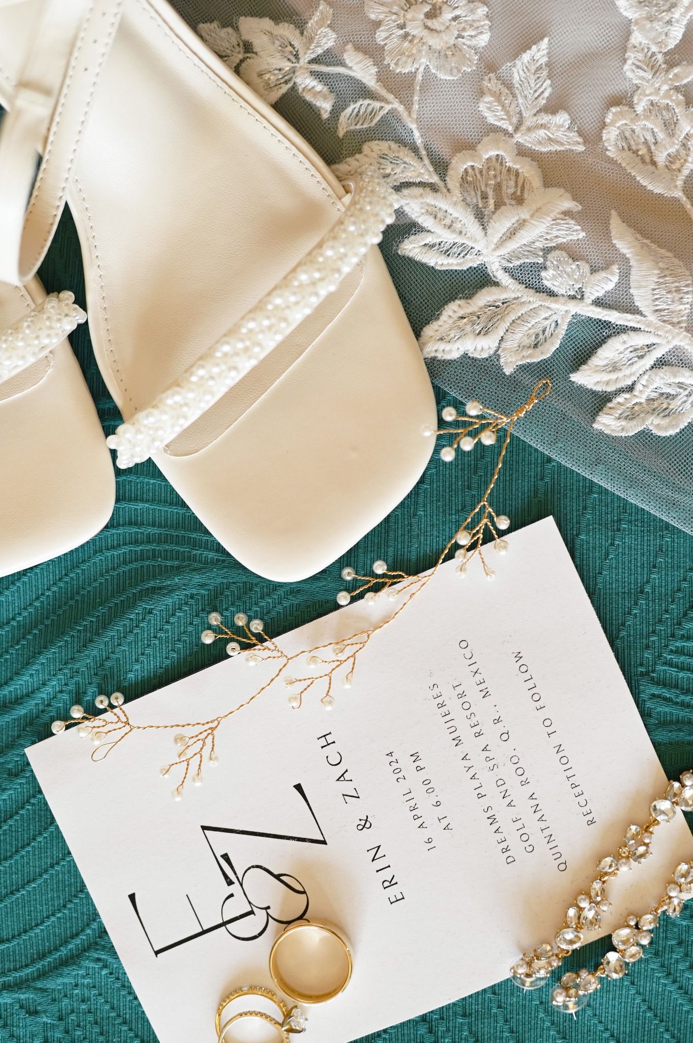 Bridal flat lay with pearl heels, Erin and Zach wedding invitation, gold rings, and lace veil.