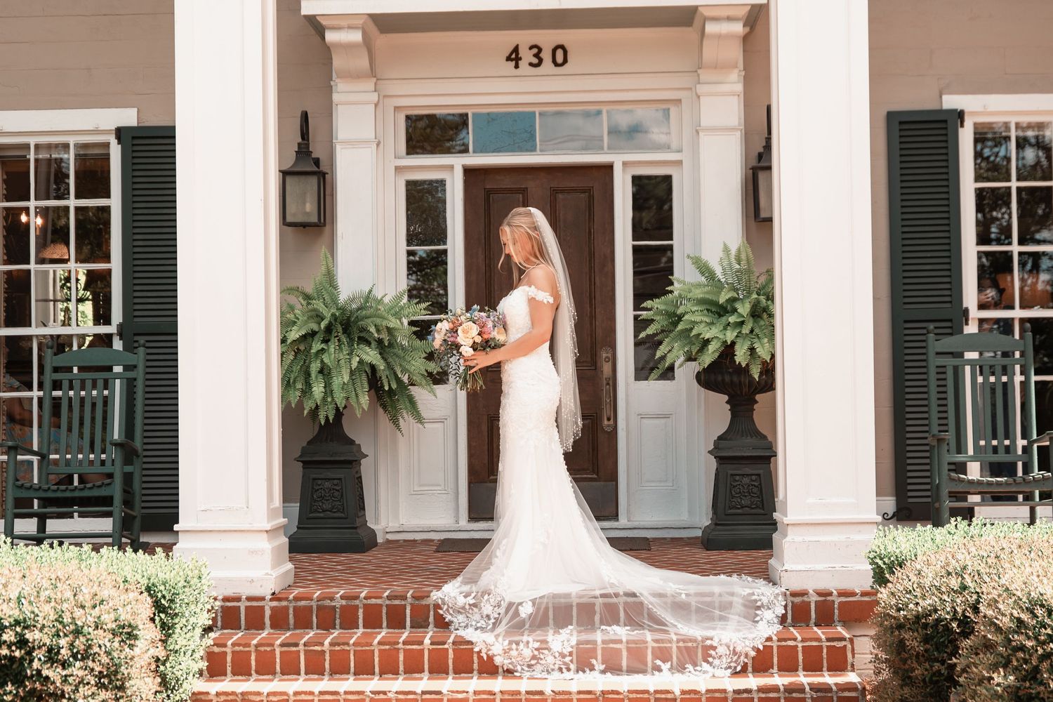 Bride in white lace gown with veil stands on brick steps of elegant Southern home entrance at 430.