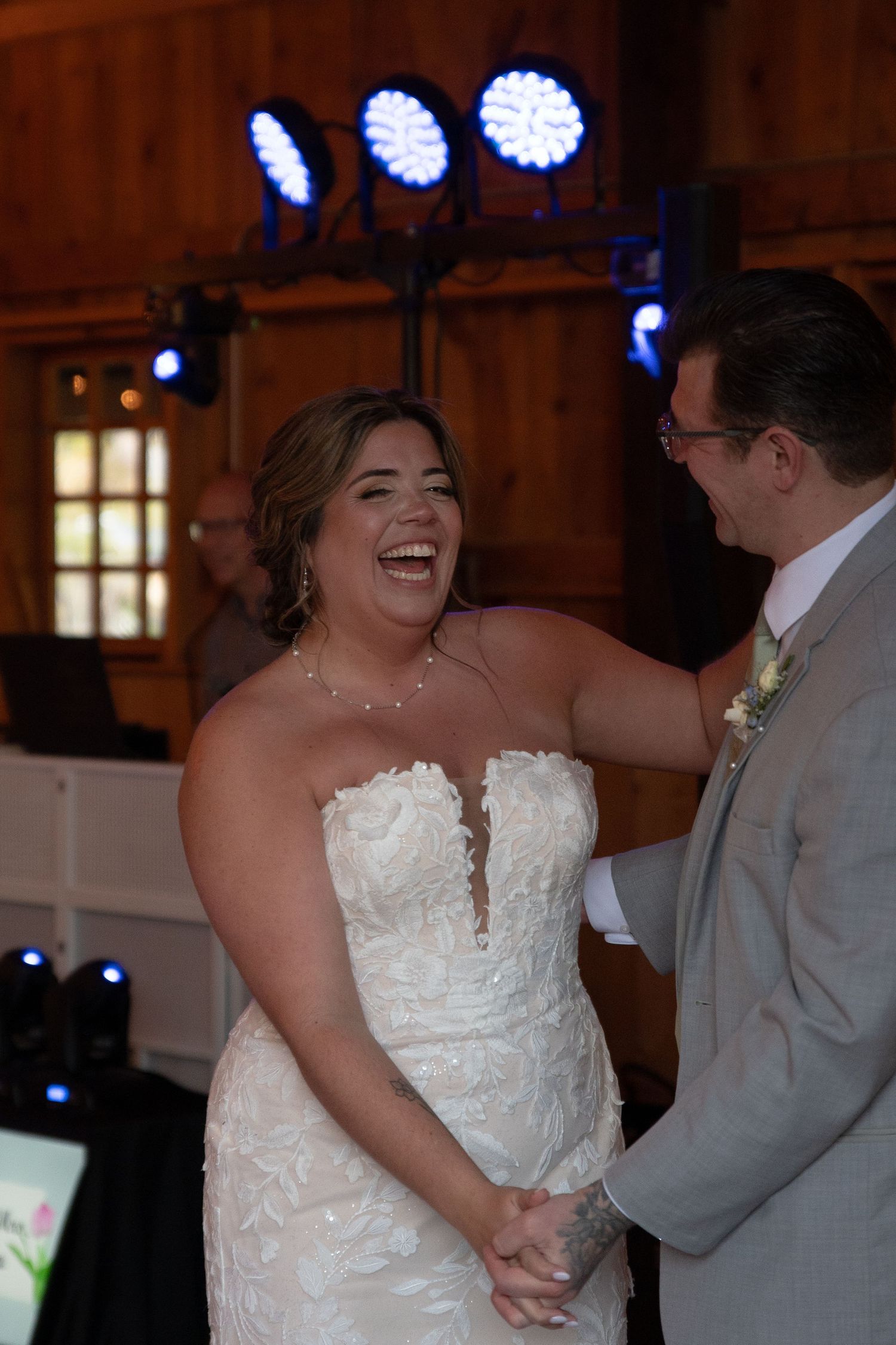 Bride in strapless lace gown laughs joyfully with groom during barn wedding reception dance.