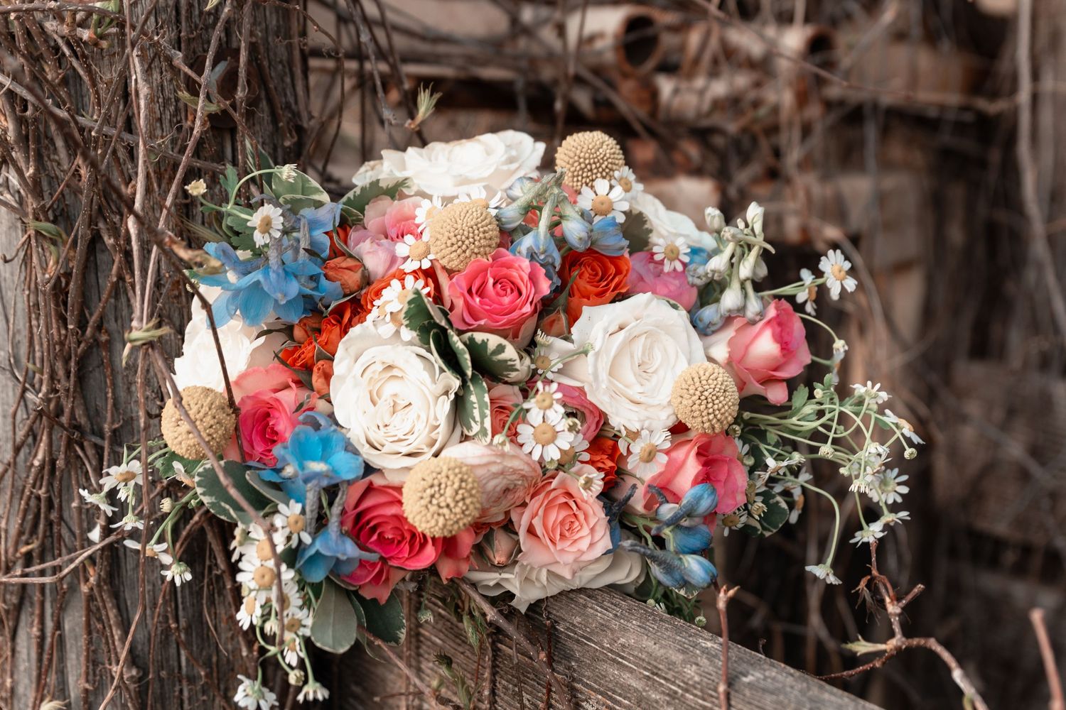 Colorful bridal bouquet with coral, white, and blue flowers on rustic wood.