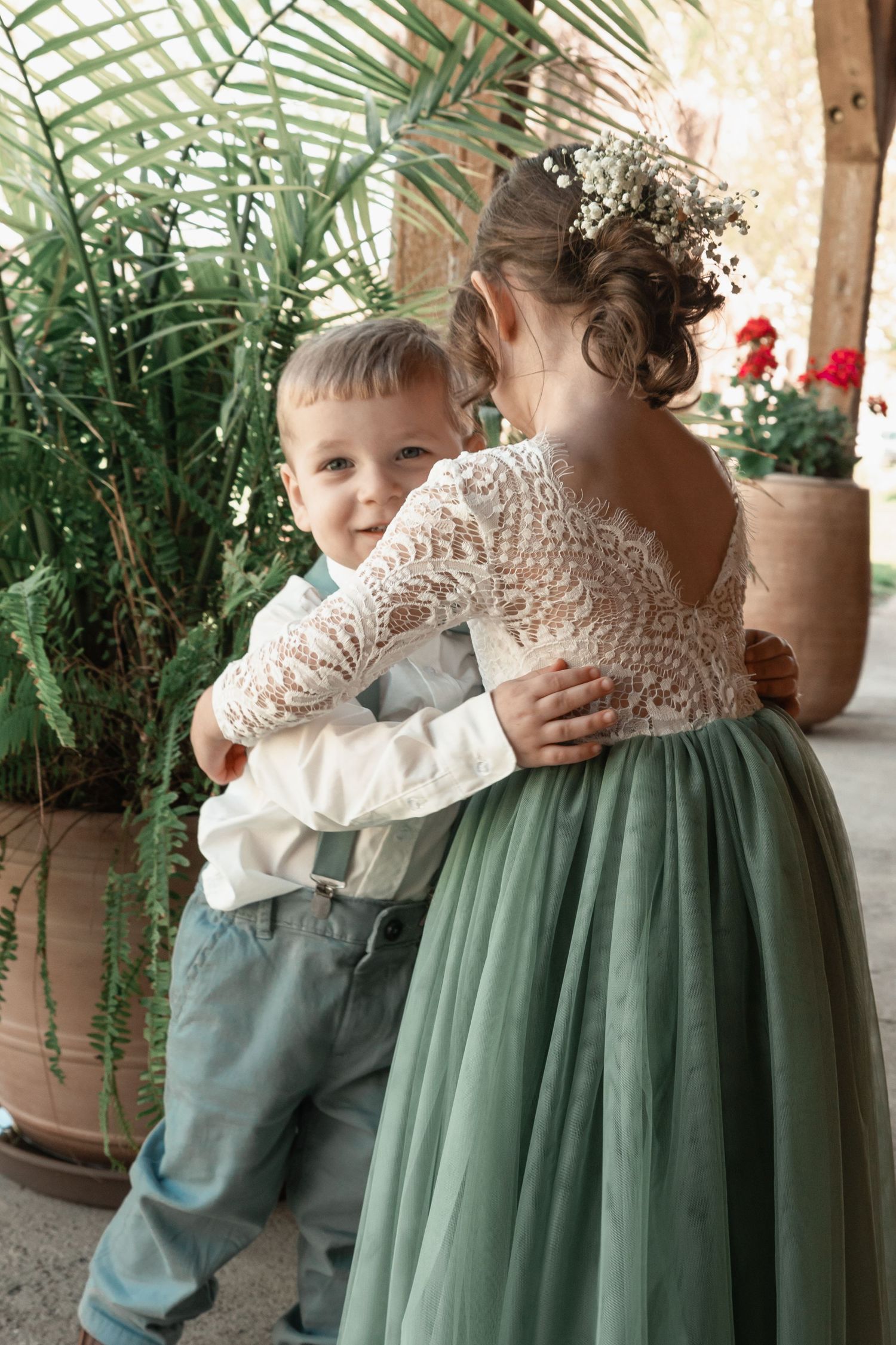 Two young children in formal wedding attire hugging near tropical plants.