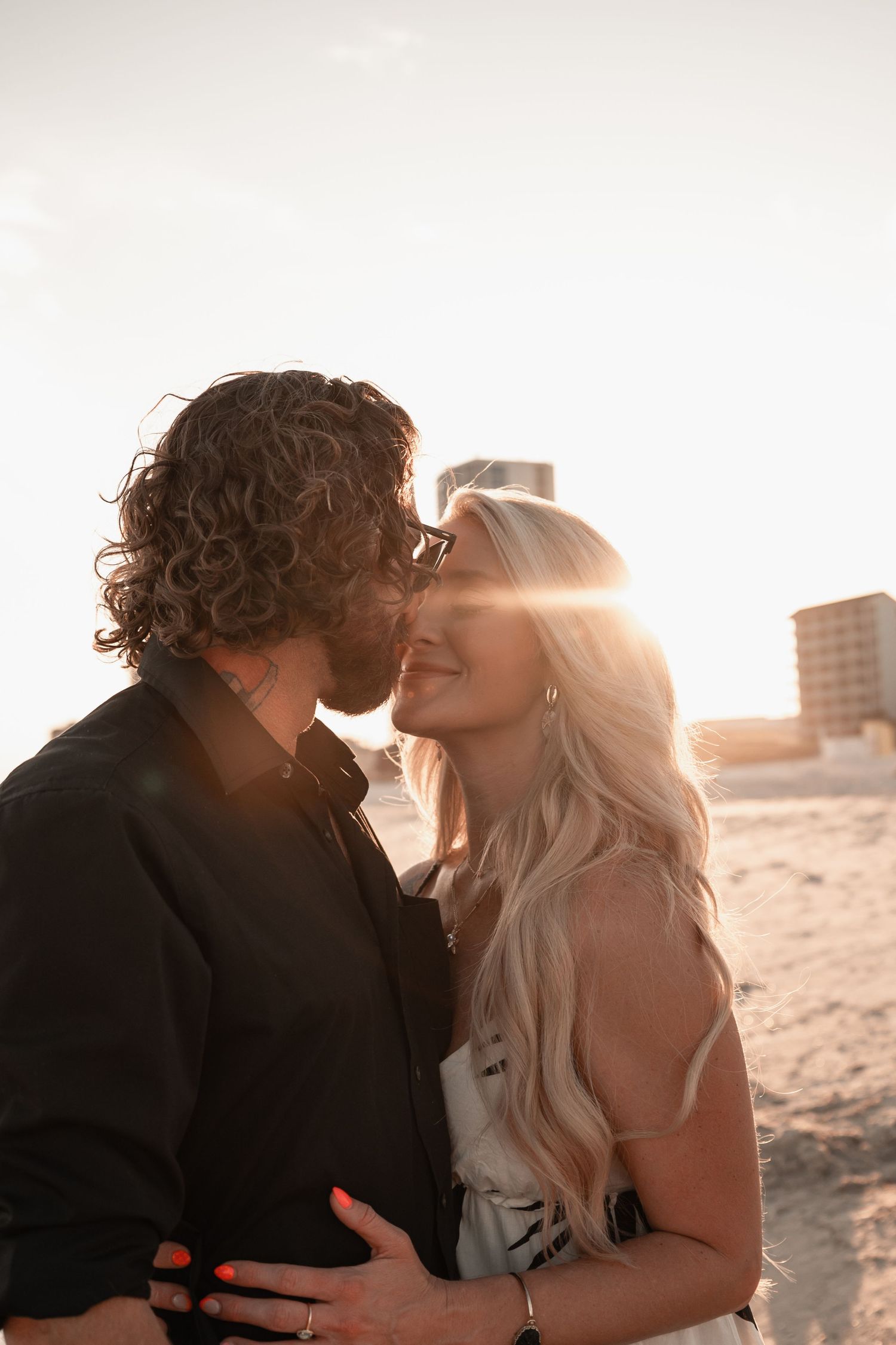 Couple sharing a romantic moment at golden hour on the beach, backlit by warm sunset light.