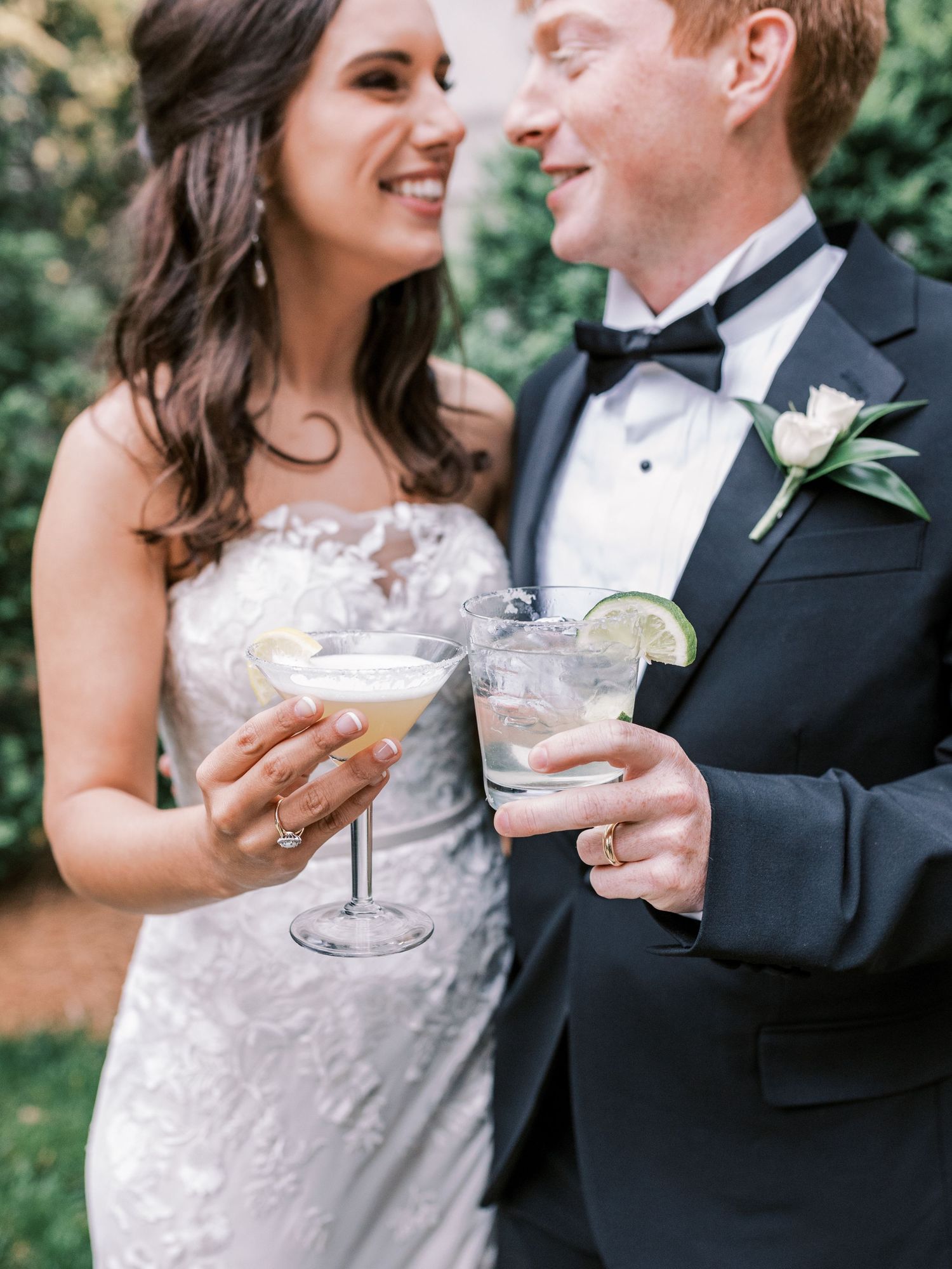 Bride with dark hair in lace wedding gown and groom in black tuxedo toast with cocktails at Swan House Gardens in Atlant