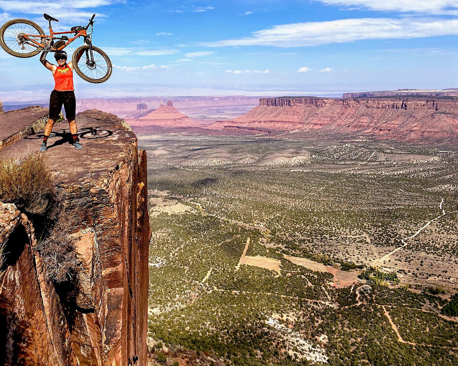A woman holding up her bike on a cliff side at Moab, Utah for the website WhiteFlamingoPhotos.com