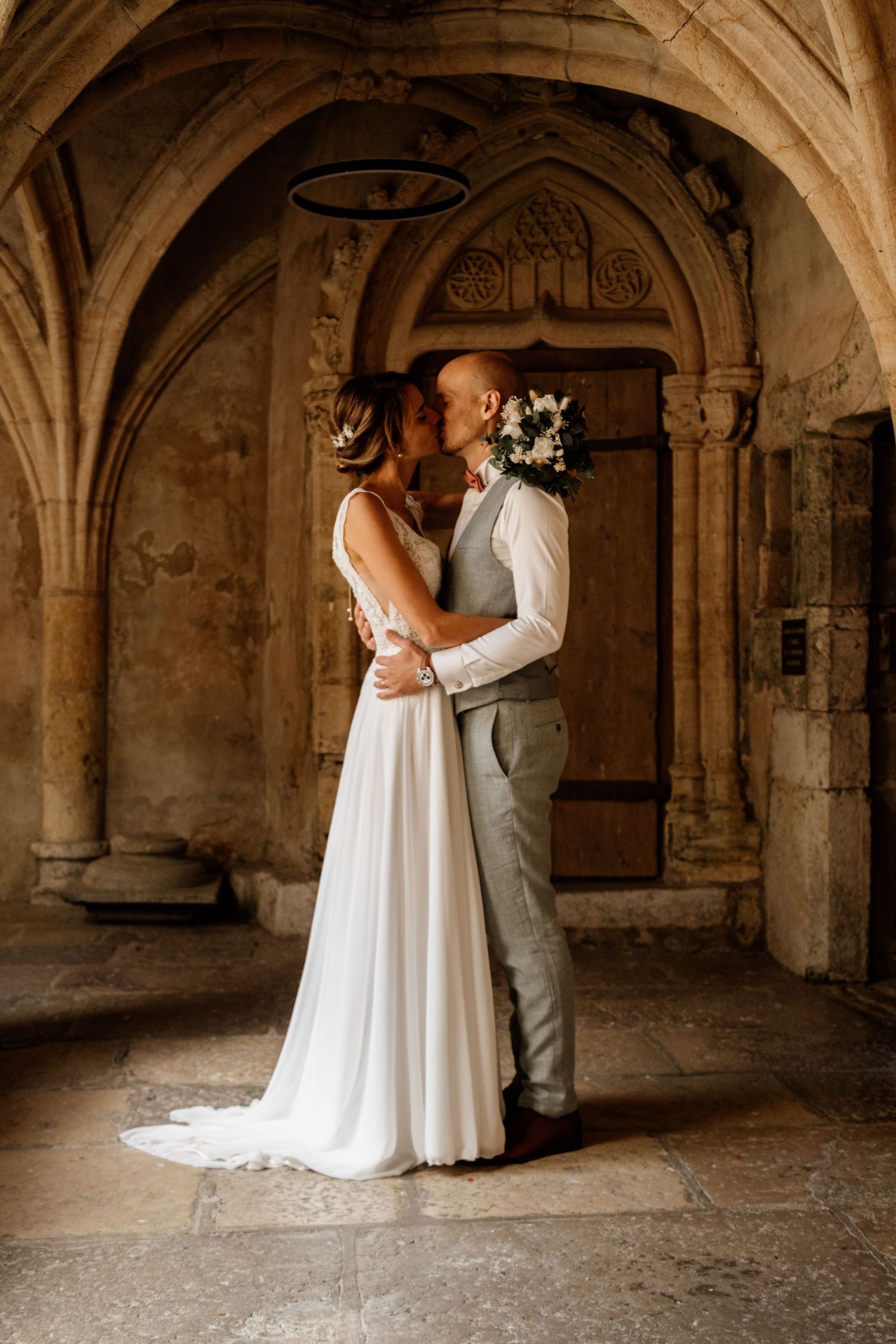 Bride and groom share a romantic kiss inside a historic stone archway with ornate carved details.
