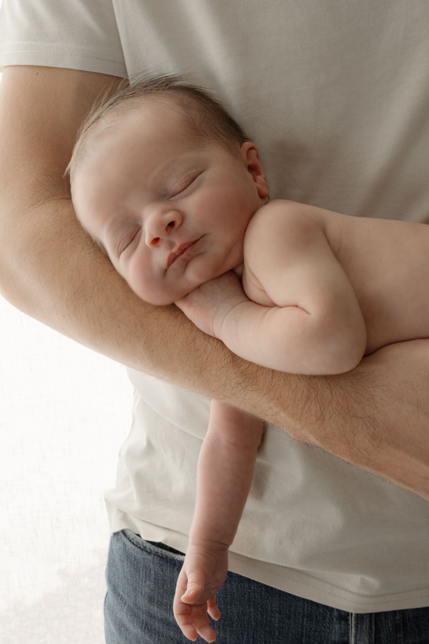 Sleeping newborn baby cradled in fathers strong arm against a white background.
