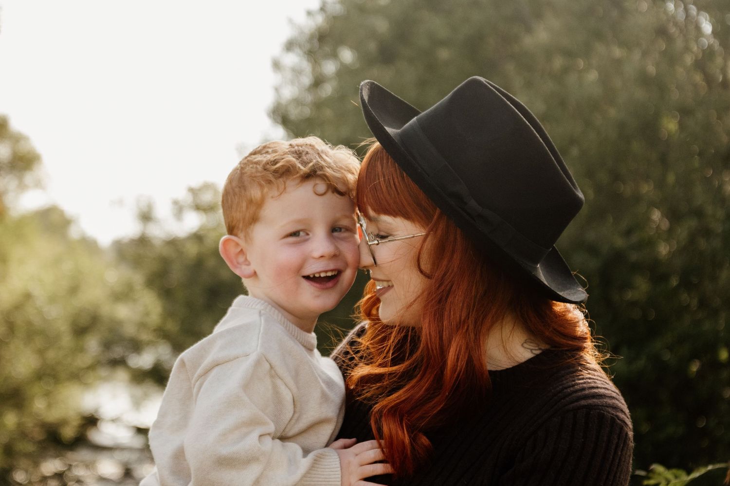 Smiling redhead mother holding her happy young son close during a golden hour outdoor portrait session.