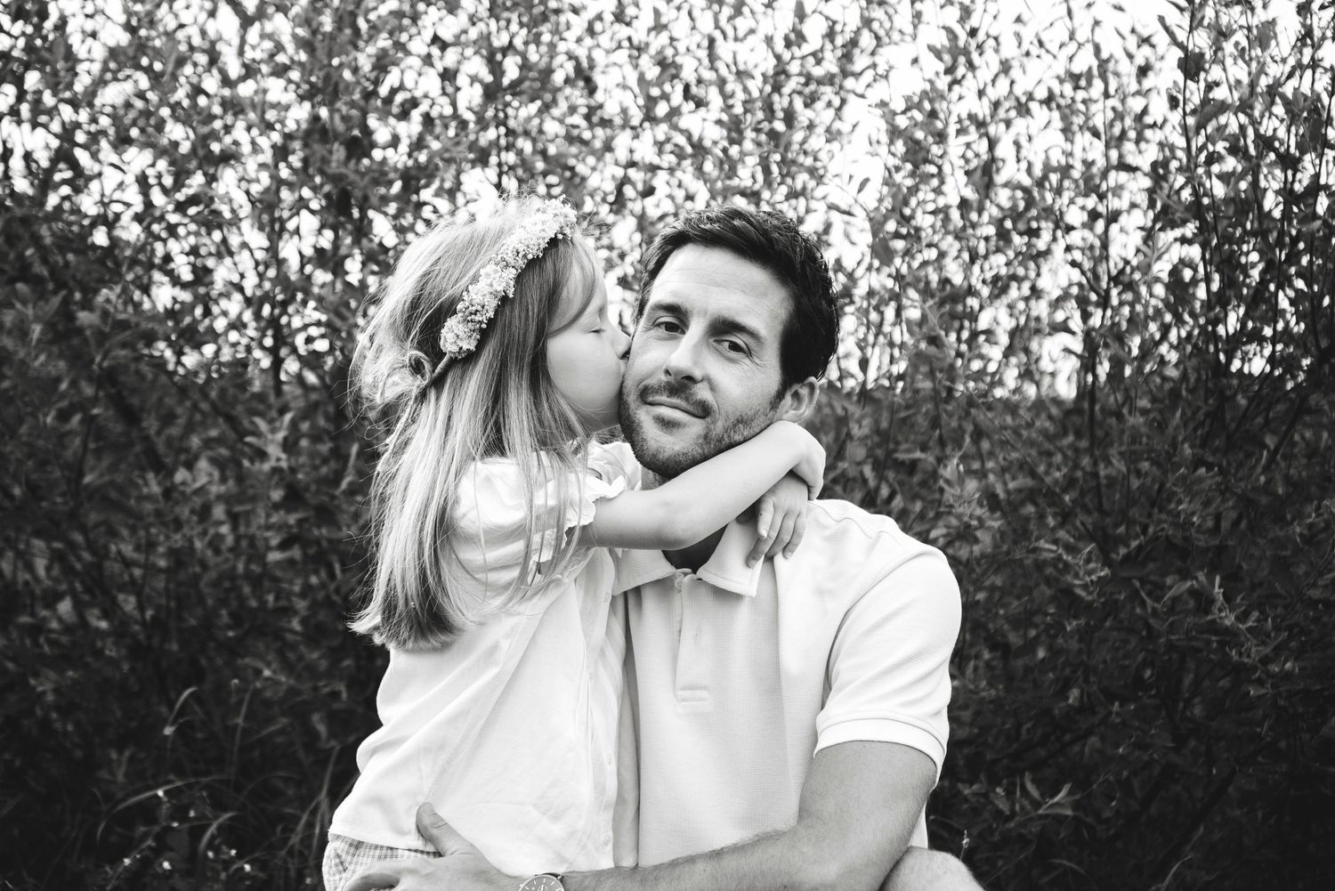 Black and white photo of a young girl kissing a smiling man on the cheek outdoors.