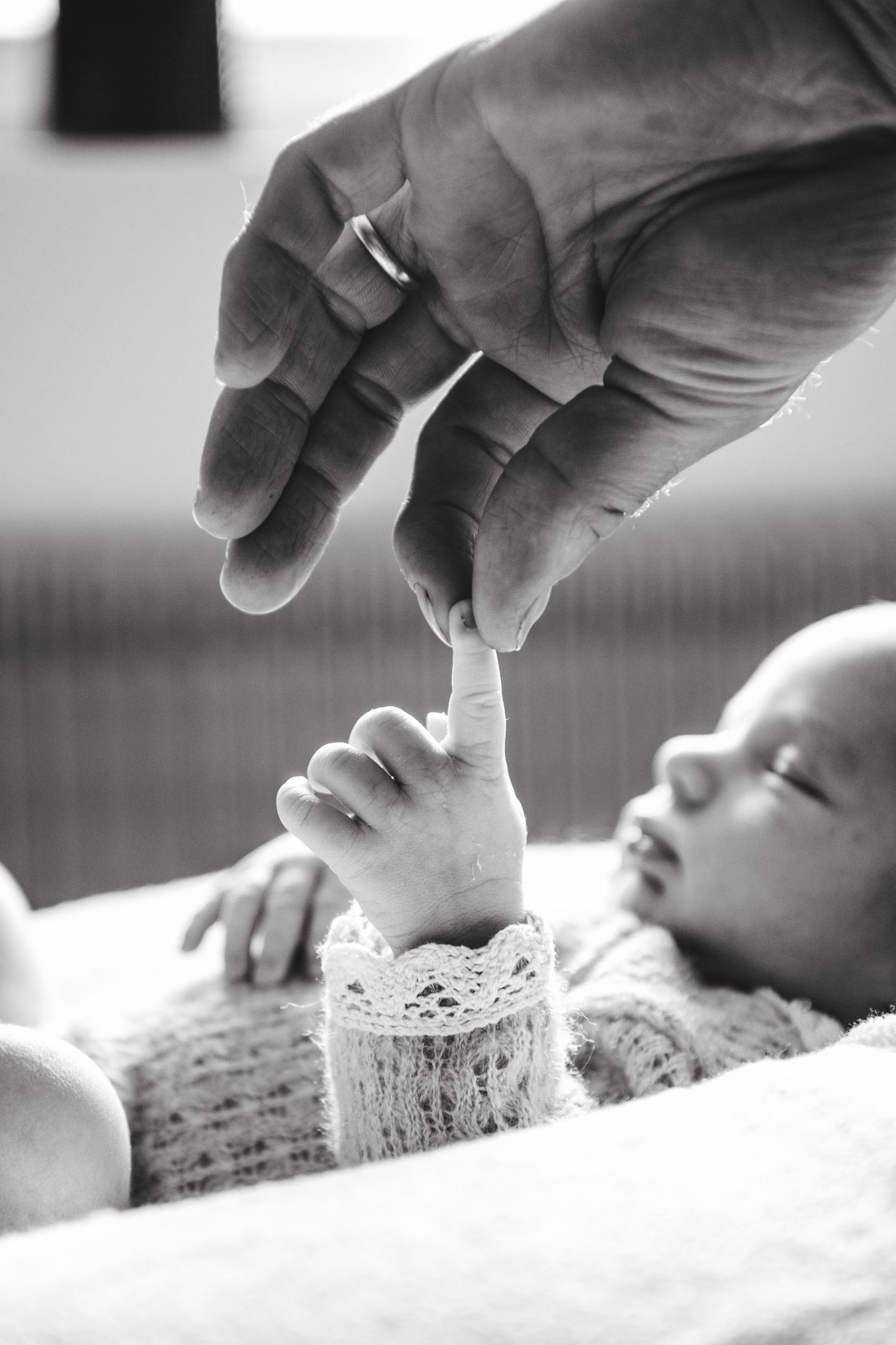 Black and white close-up of a newborn baby grasping an adult finger with tiny hand.