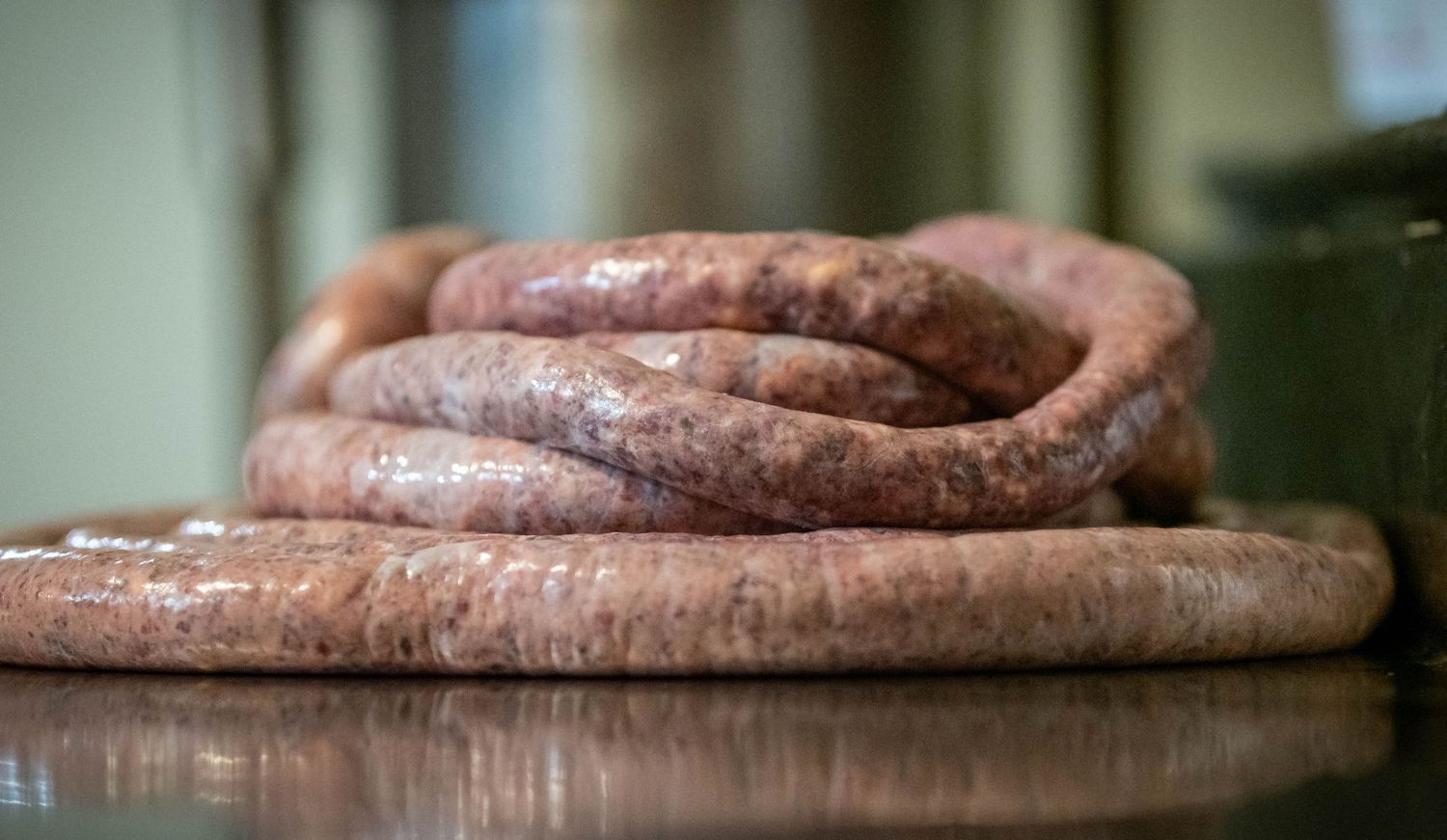 Raw homemade sausage links coiled on a wooden cutting board with shallow depth of field.