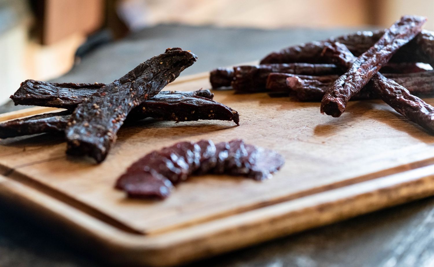 Dark beef jerky strips arranged on a wooden cutting board.