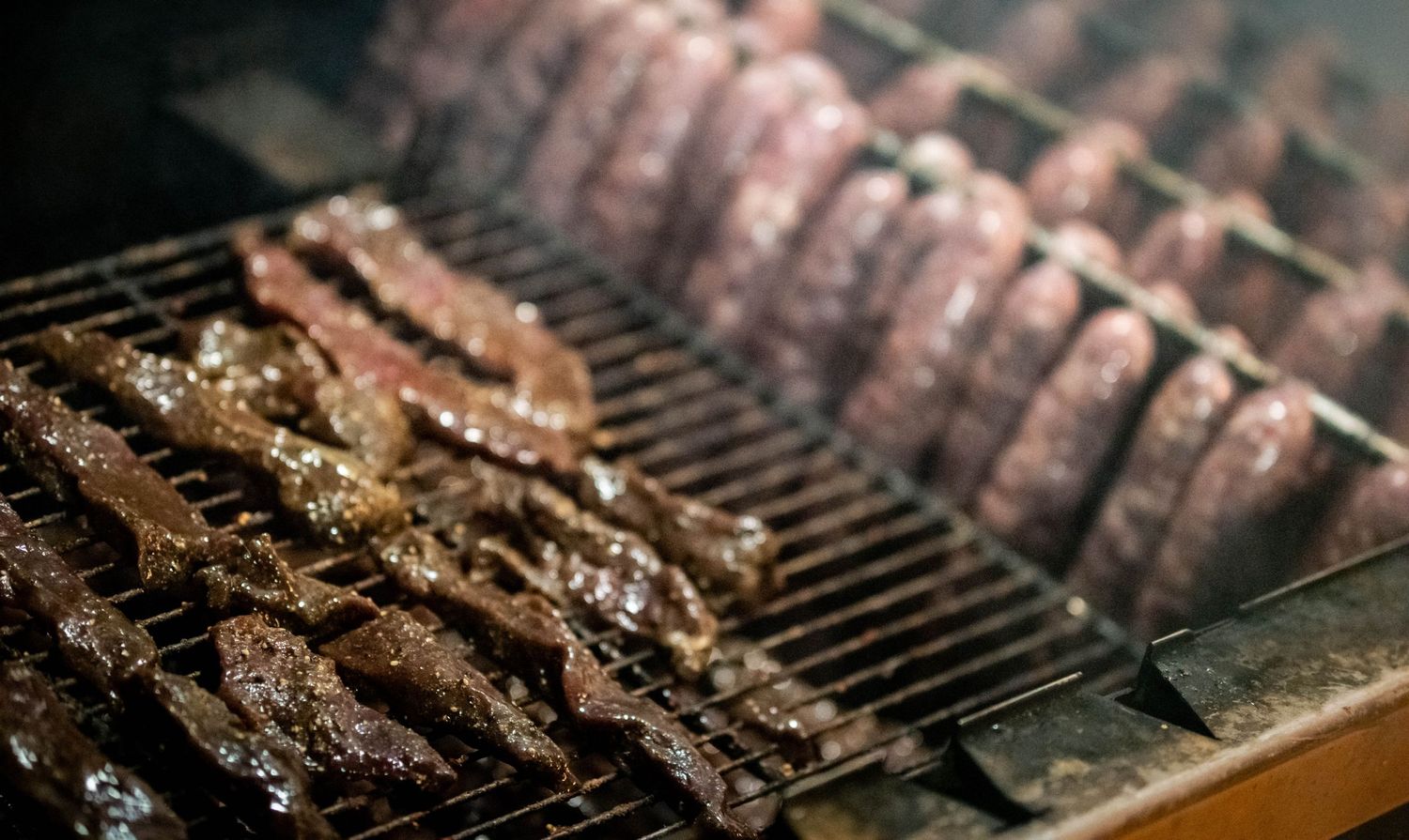 Marinated meat strips cooking on a grill rack.